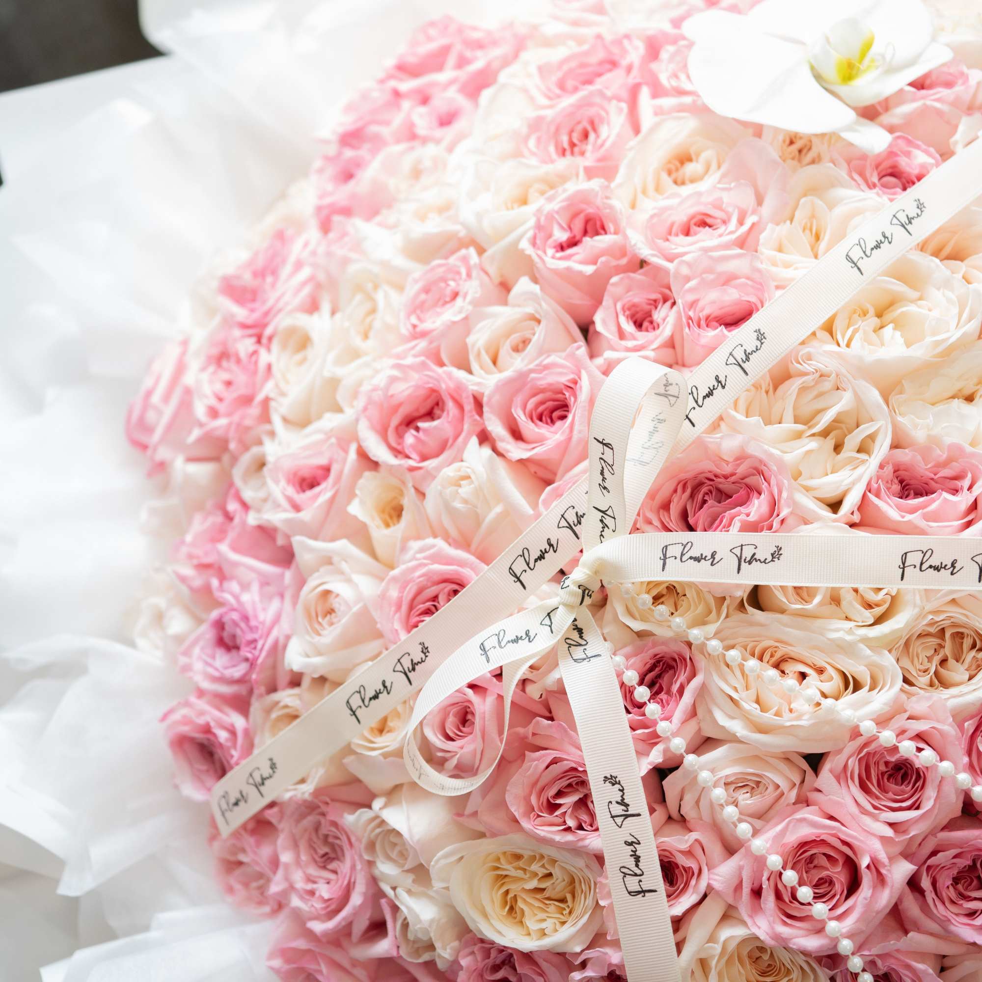 Large bouquet of pink and cream roses wrapped in white paper with ribbon