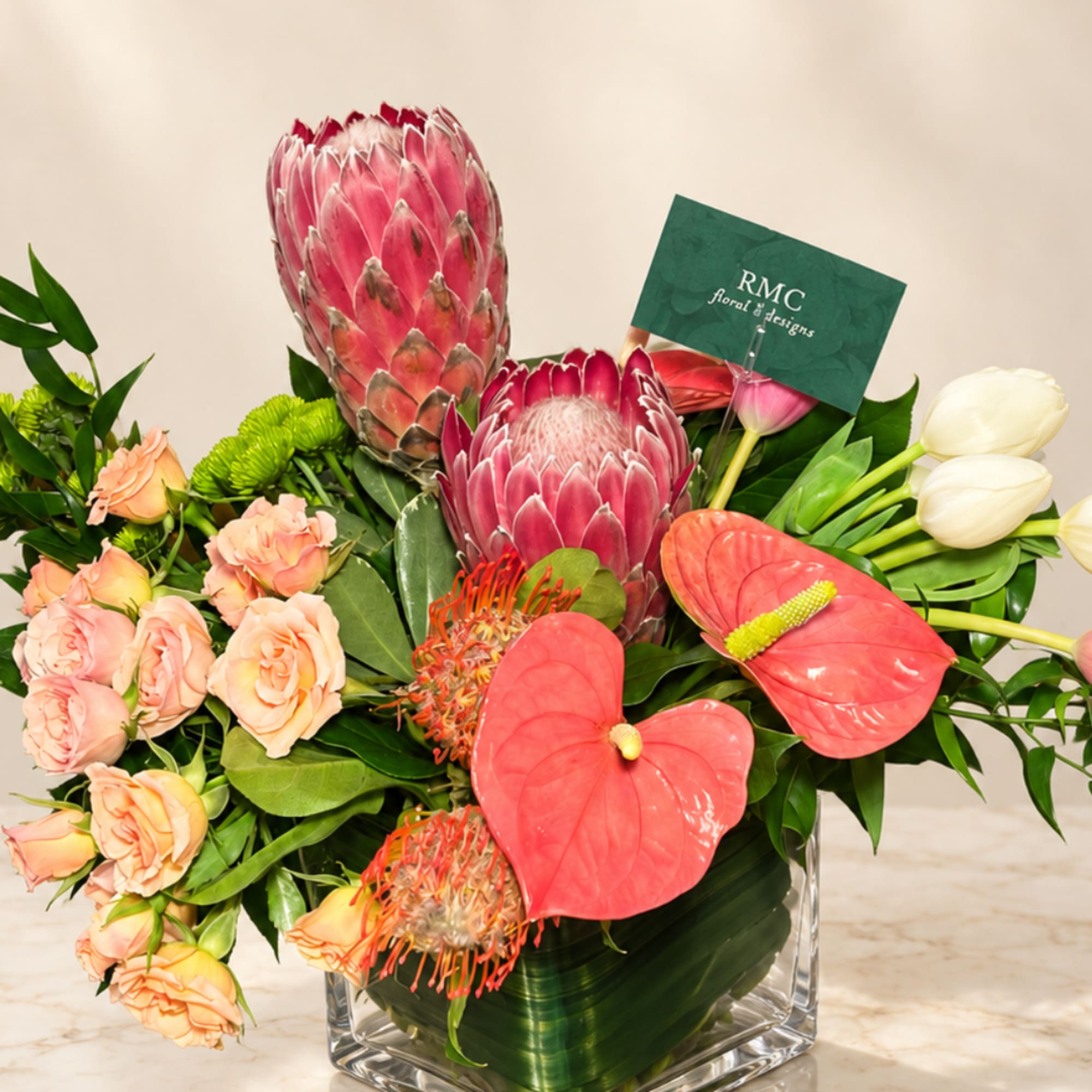 Mixed bouquet with pink protea, coral roses, red anthuriums, and white tulips in a glass vase