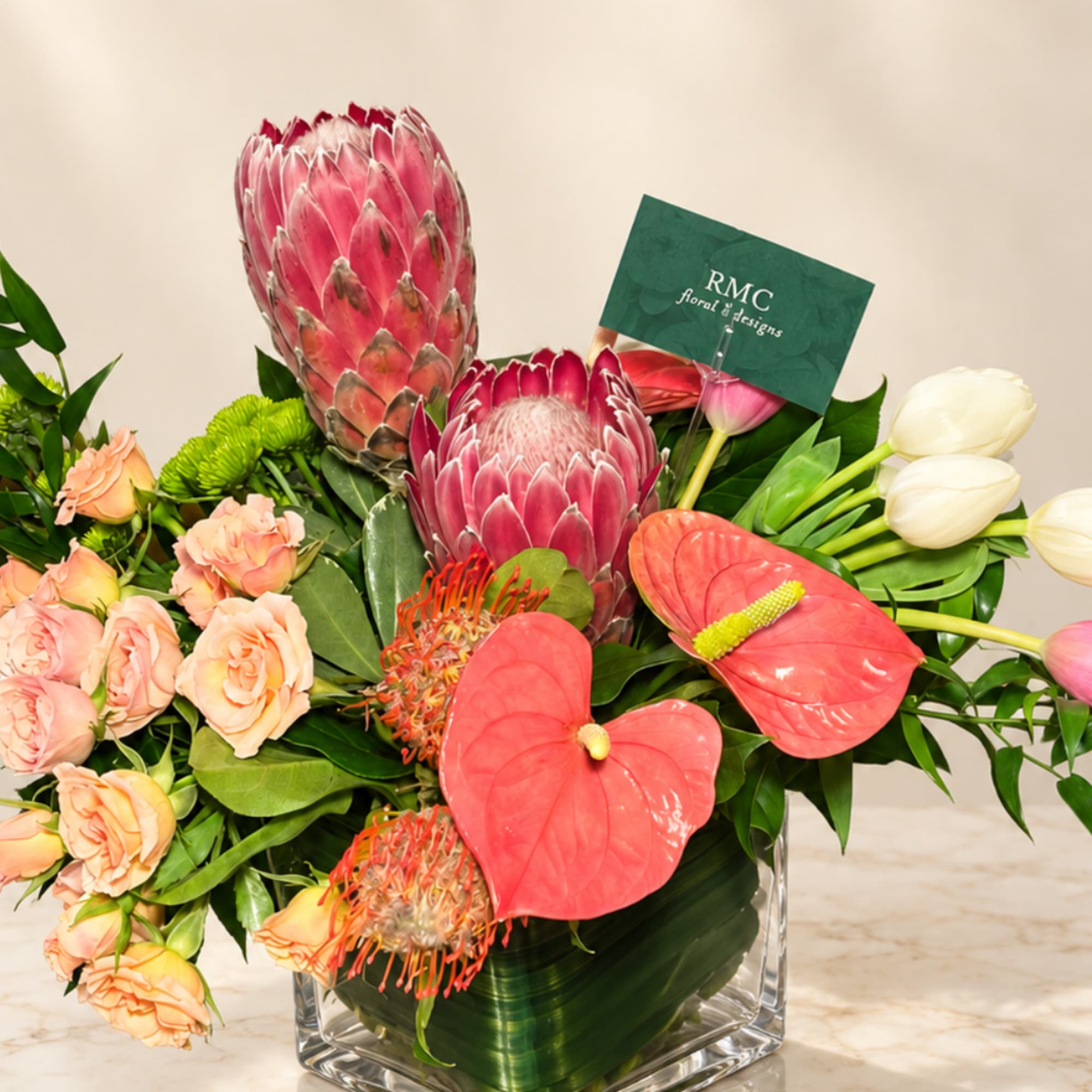 Mixed tropical bouquet with protea, anthurium, roses, and tulips in a clear vase