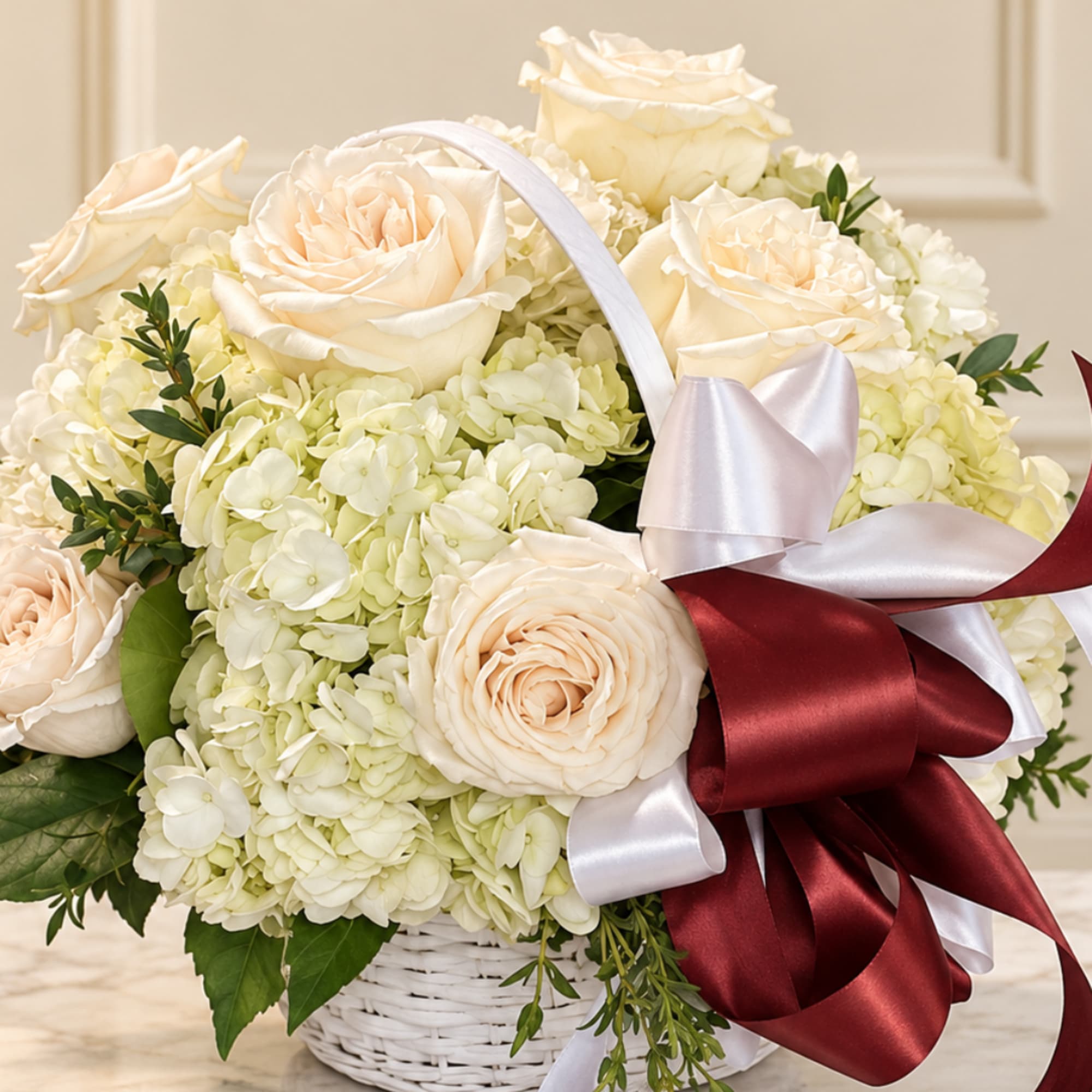 Cream roses and hydrangeas in a white basket with a burgundy ribbon
