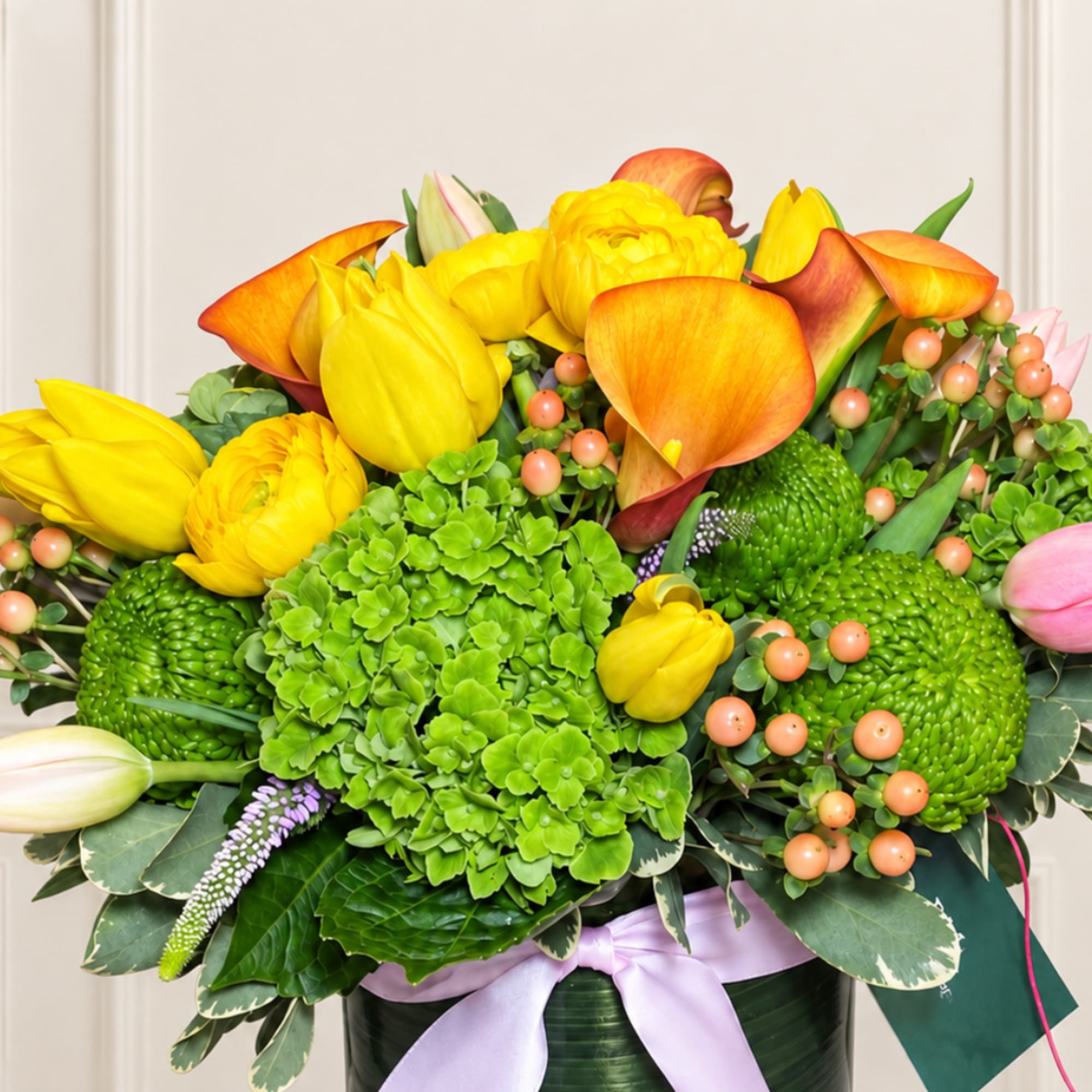 Bright yellow and orange floral arrangement in a dark vase with a lavender ribbon