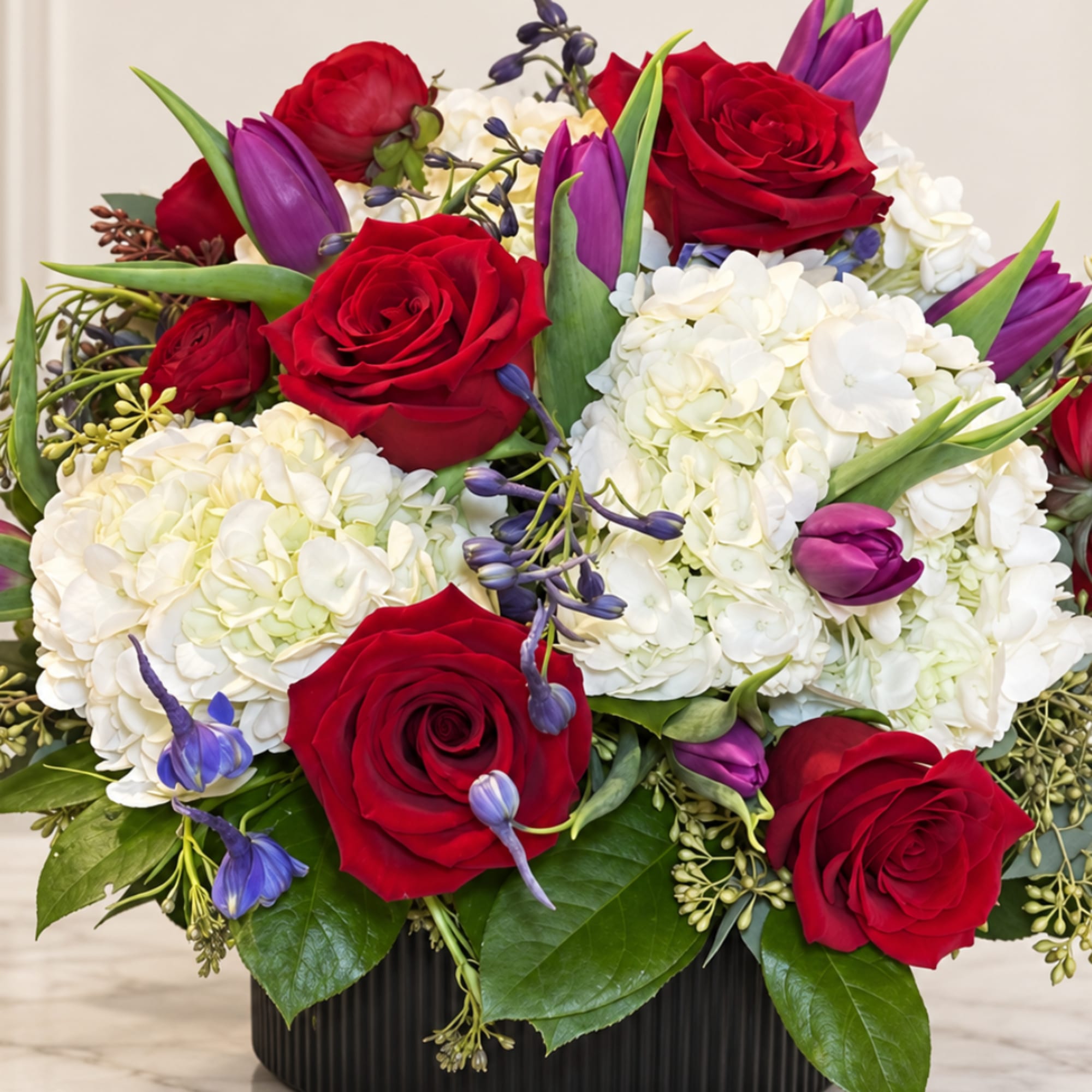 Bouquet of red roses, white hydrangeas, and purple tulips in a black vase