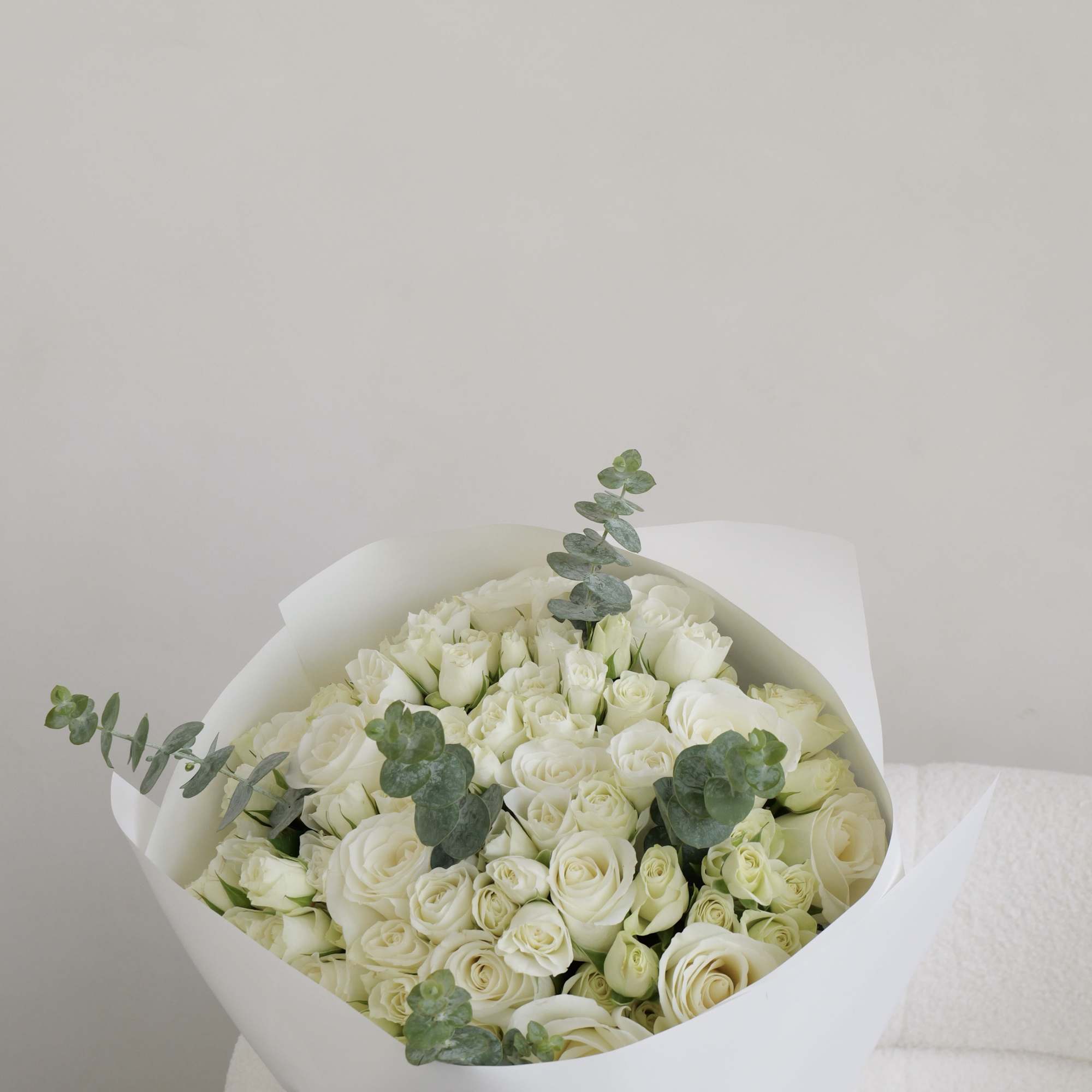 Bouquet of white roses wrapped in white paper with eucalyptus accents