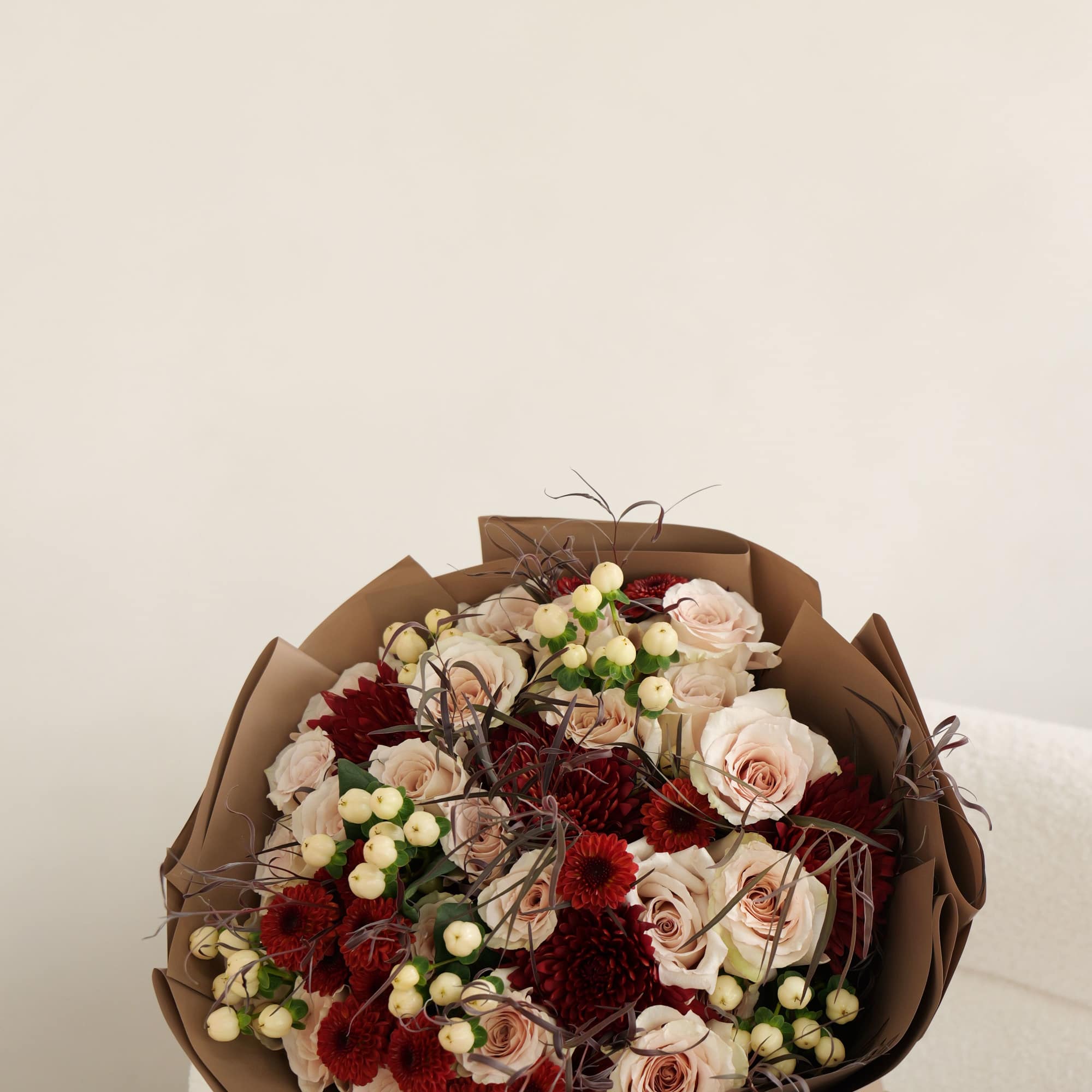 Bouquet of blush roses and red chrysanthemums wrapped in brown paper