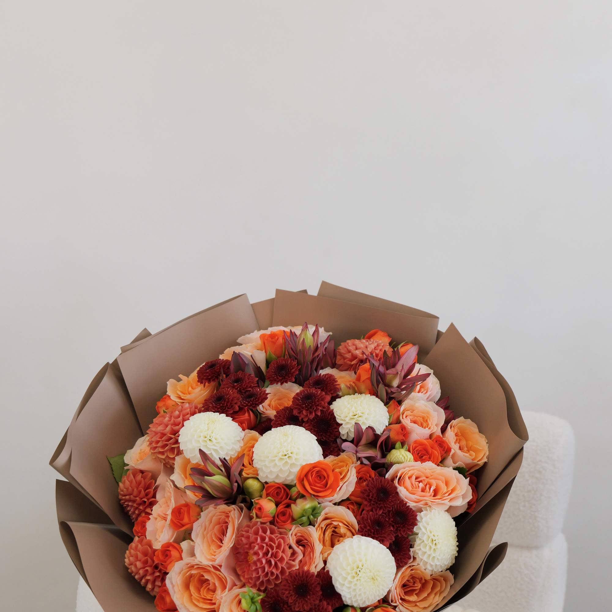 Bouquet of orange, peach, white, and burgundy flowers wrapped in brown paper