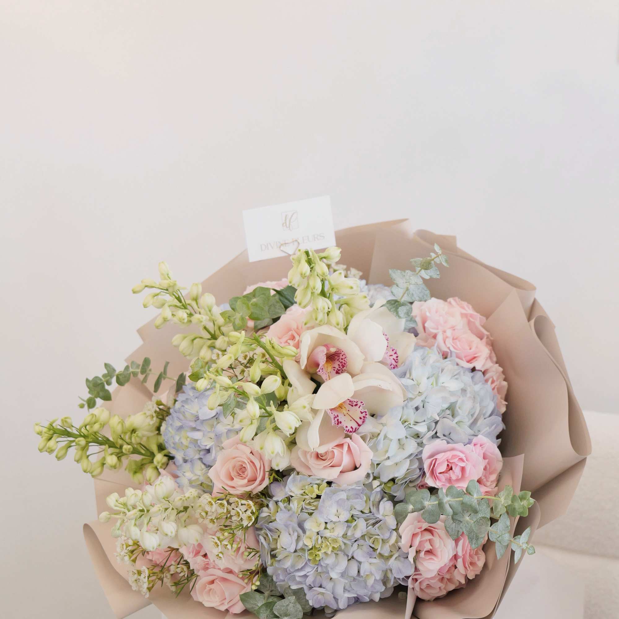 Pastel bouquet of pink roses, blue hydrangeas, and white orchids wrapped in beige paper