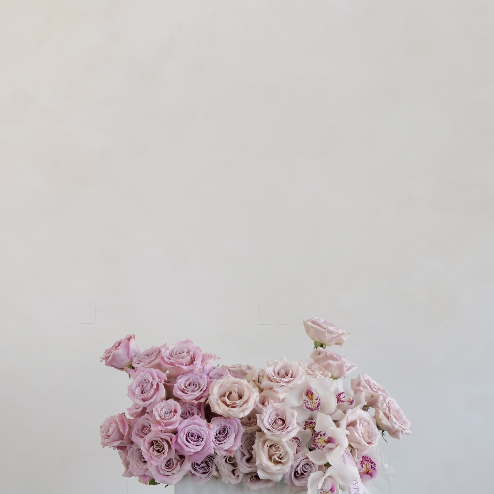 Pink and lavender roses arranged in a white vase with white orchids