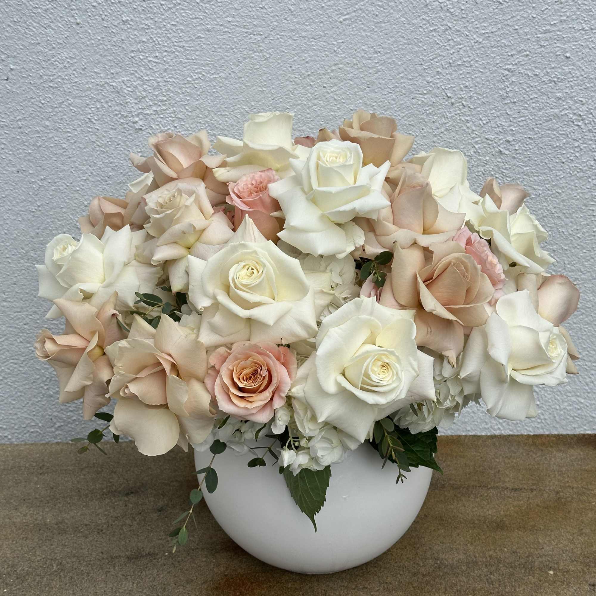 Cream and blush roses arranged in a white bowl vase