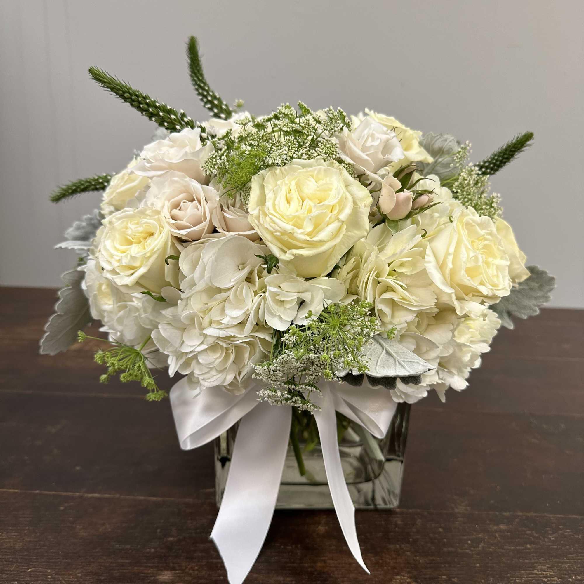 Cream rose and hydrangea arrangement in a square glass vase with a white ribbon