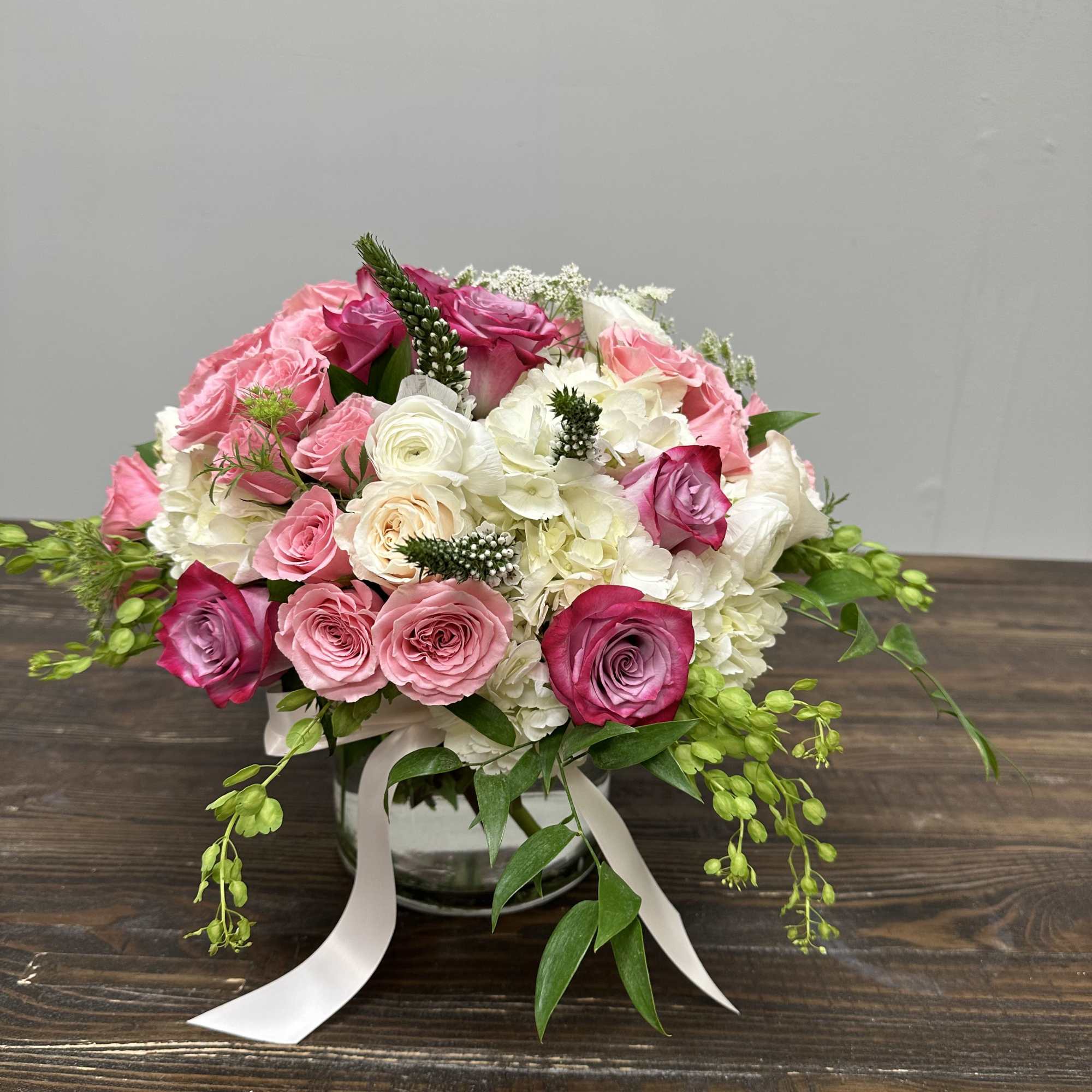Pink and white rose bouquet in a glass vase with ribbon