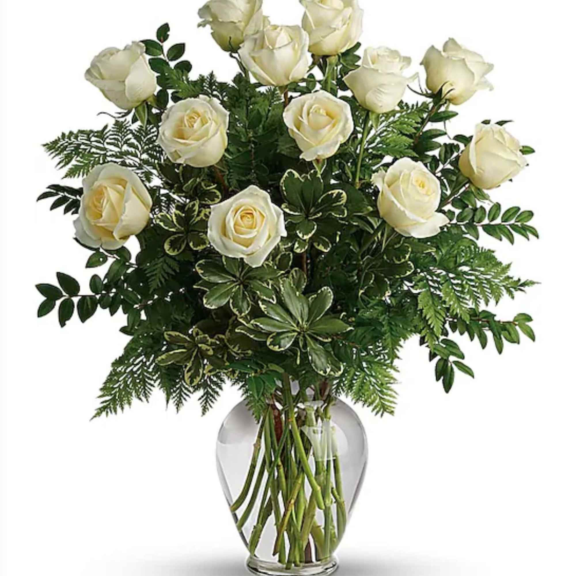 White roses arranged in a clear glass vase with mixed greenery