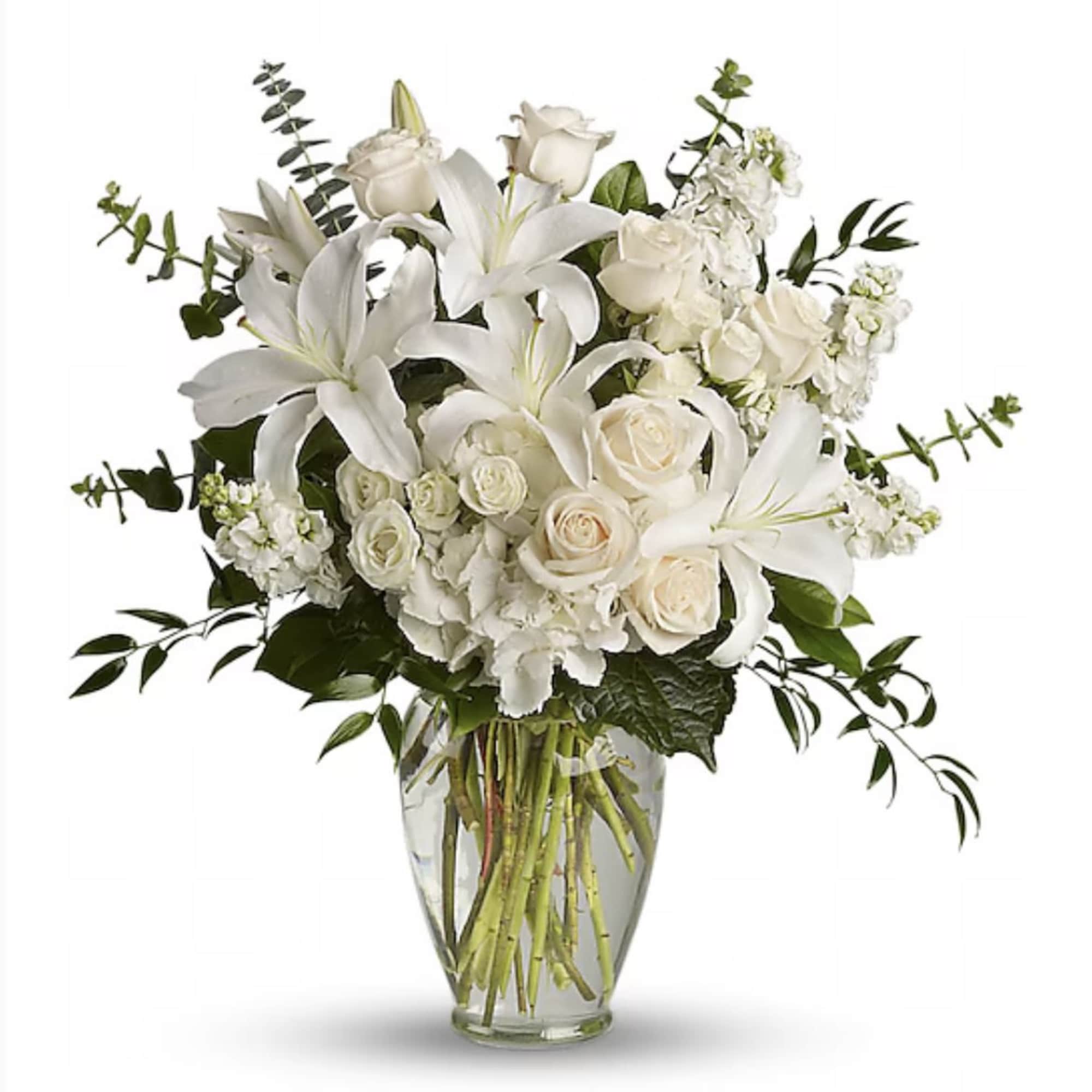 Tall white arrangement of lilies, roses, and hydrangeas in a clear glass vase