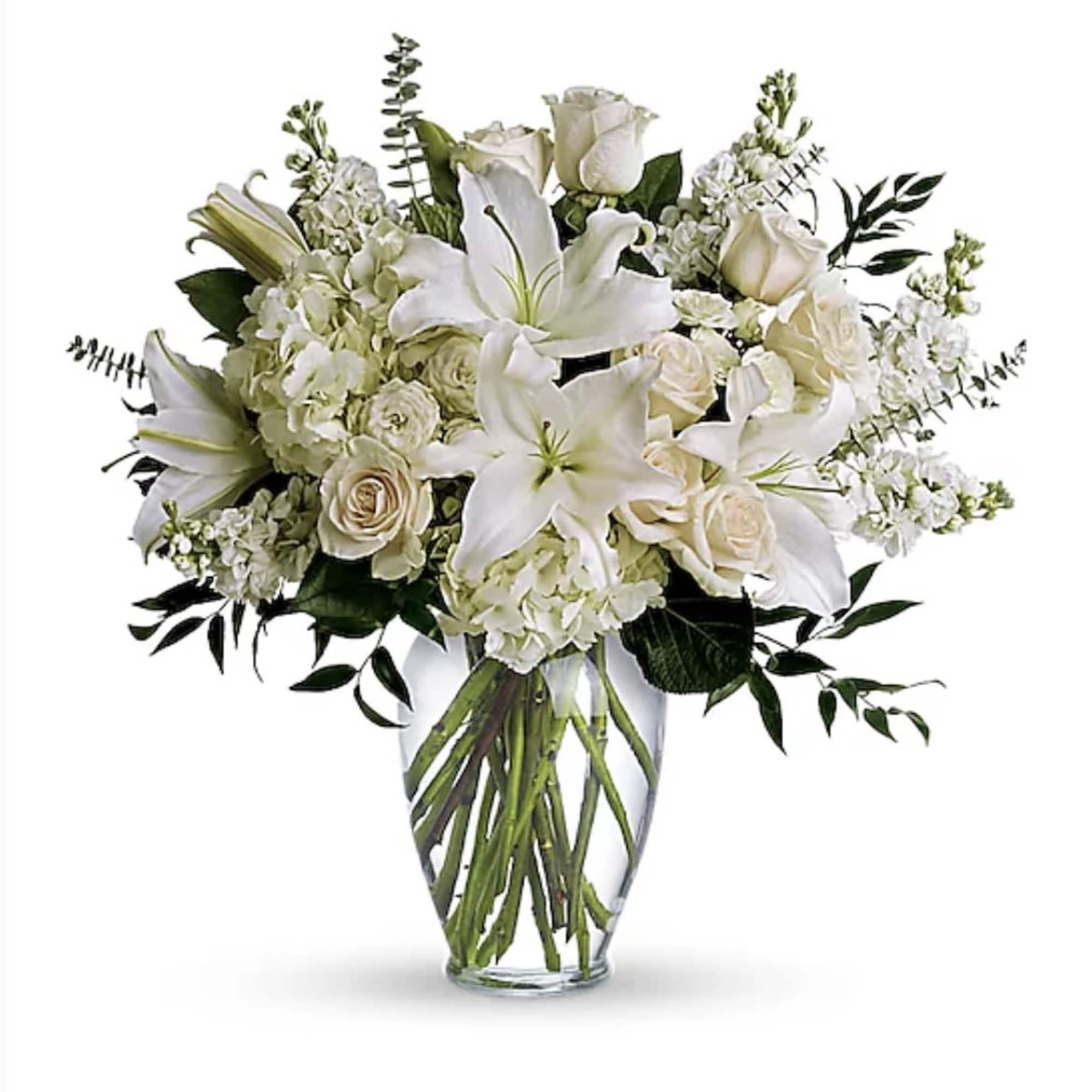 All-white arrangement of lilies, roses, and hydrangeas in a clear glass vase