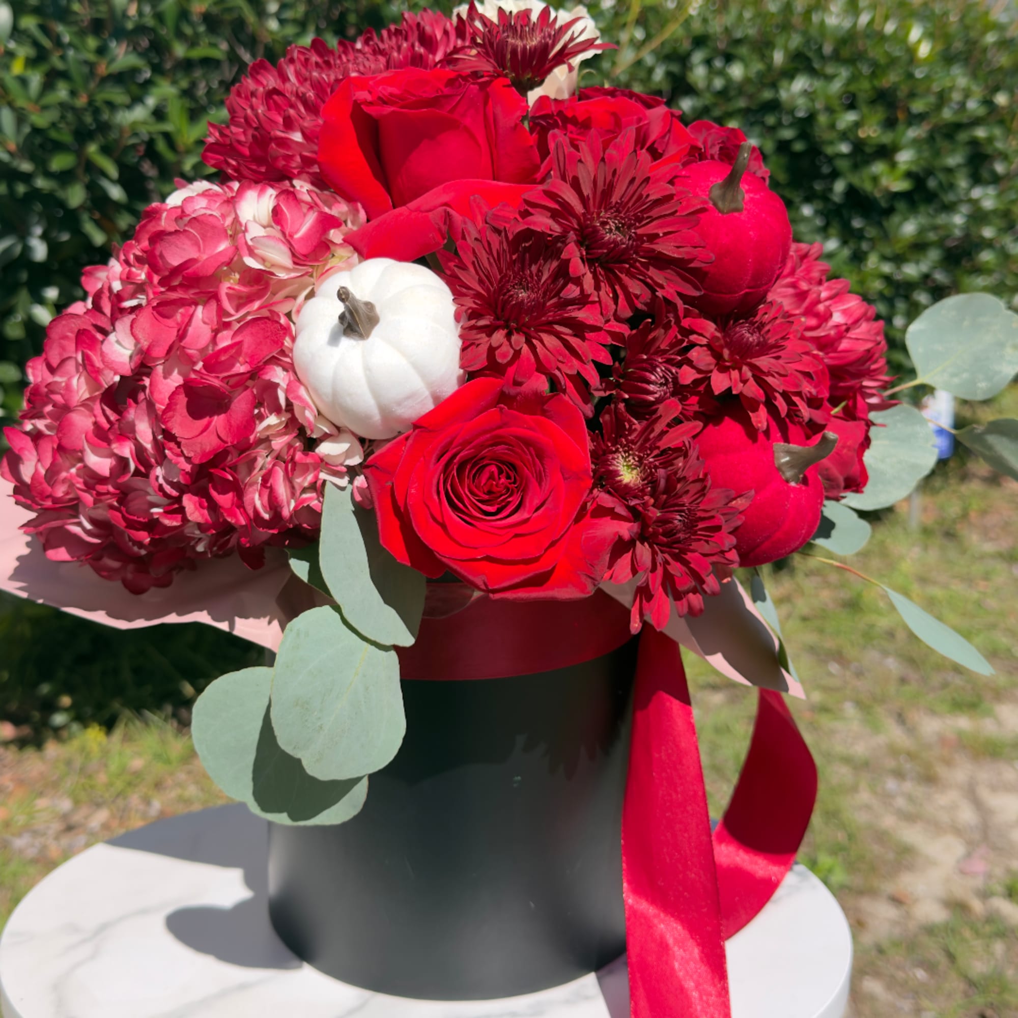Red roses and burgundy mums in a black hatbox with a red ribbon