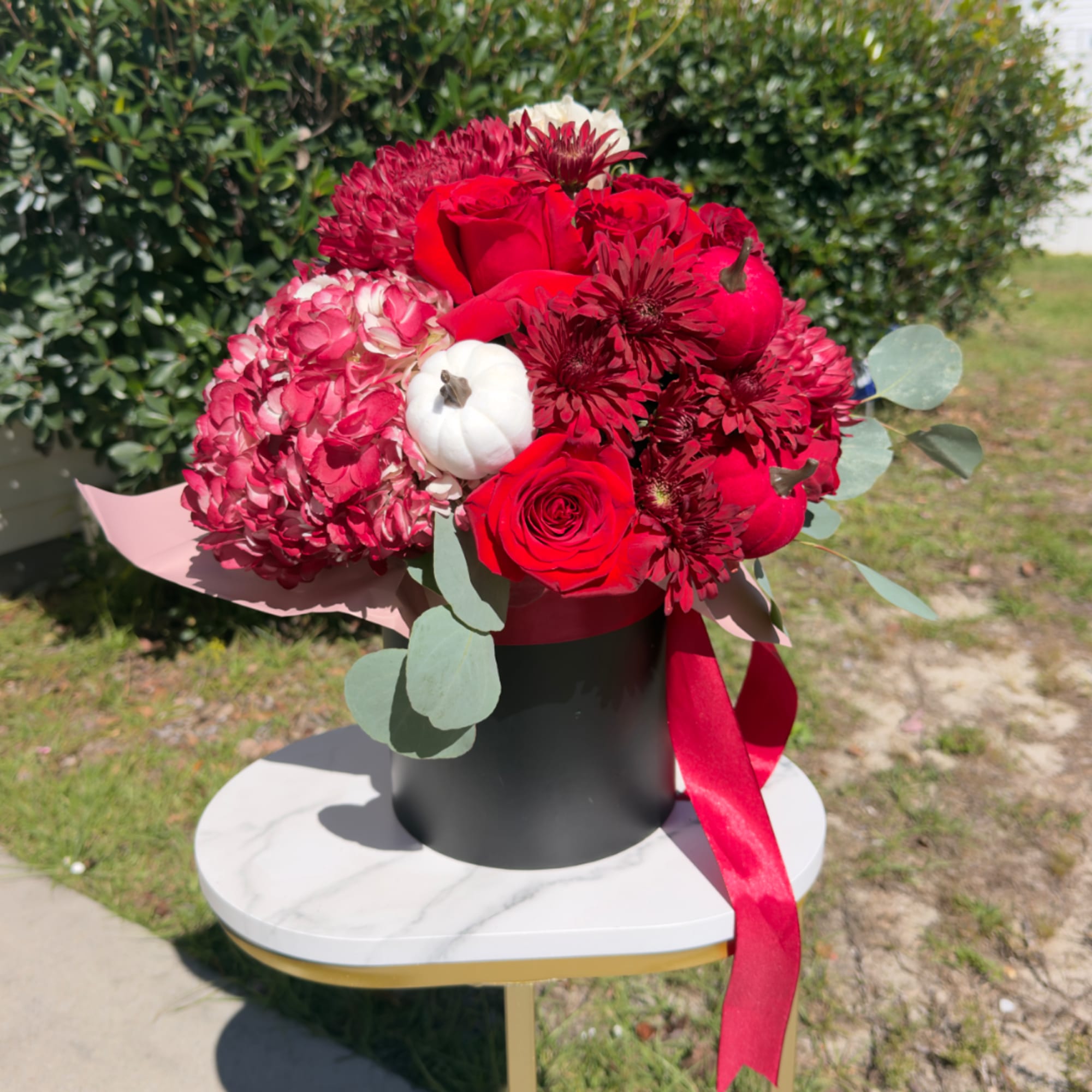 Red roses and burgundy blooms in a black hatbox with a red ribbon