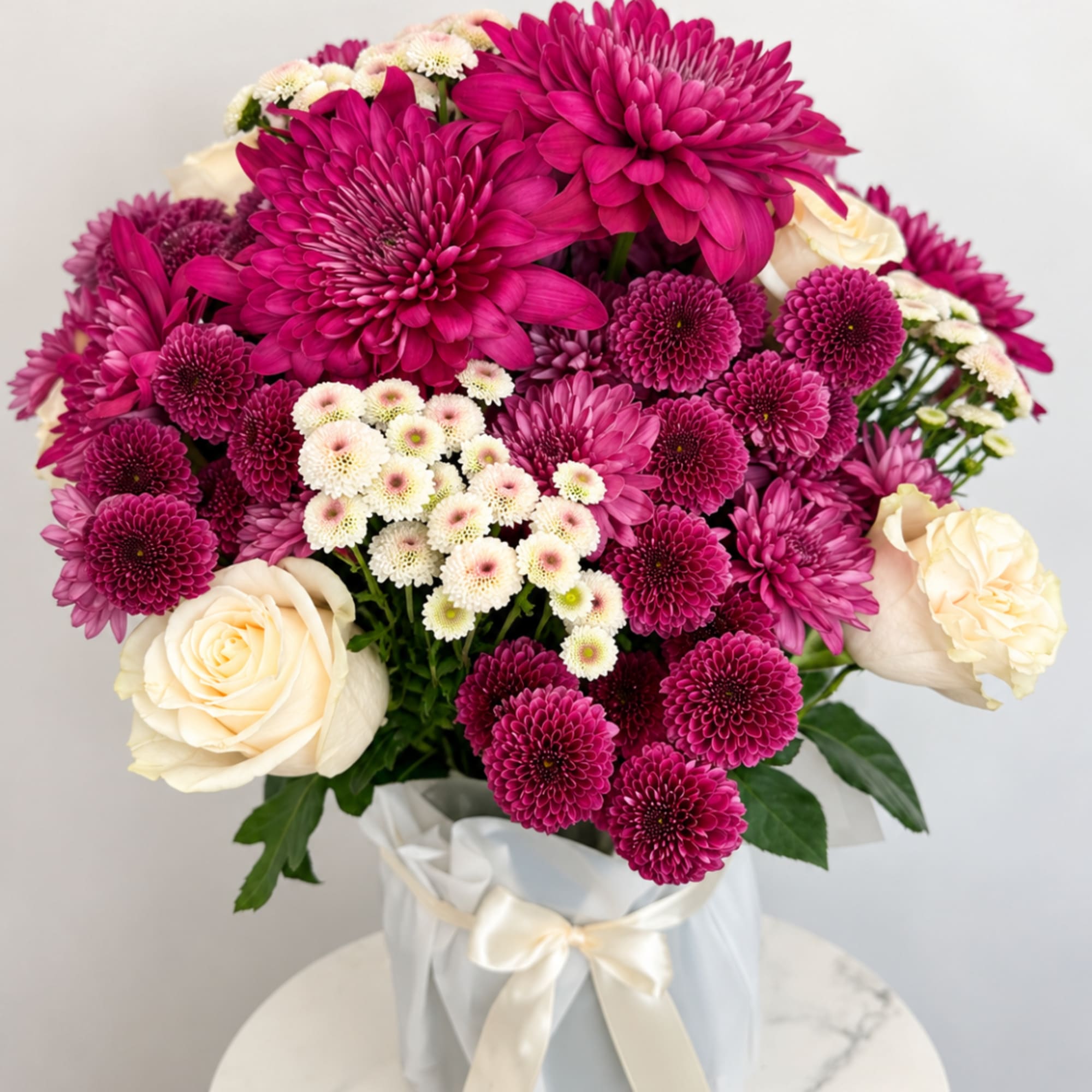 Magenta chrysanthemums and cream roses in a white wrapped vase arrangement