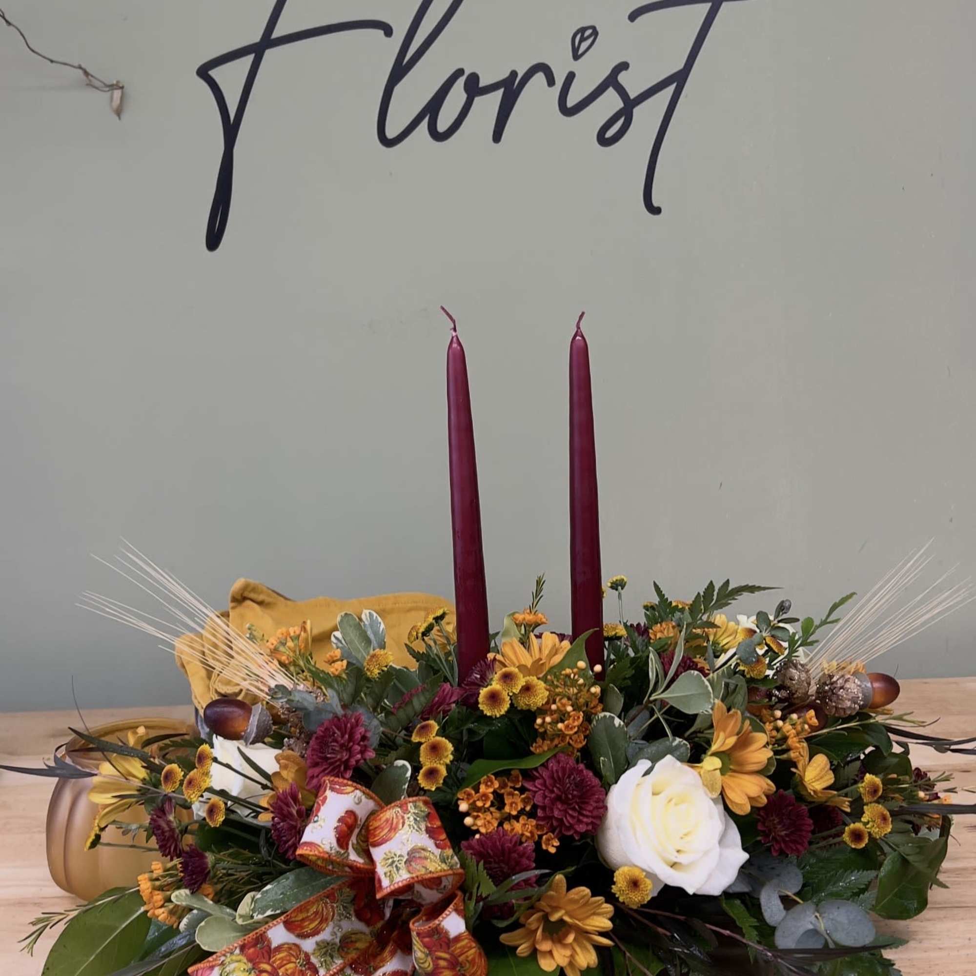 Autumn floral centerpiece with two burgundy candles and a ribbon bow