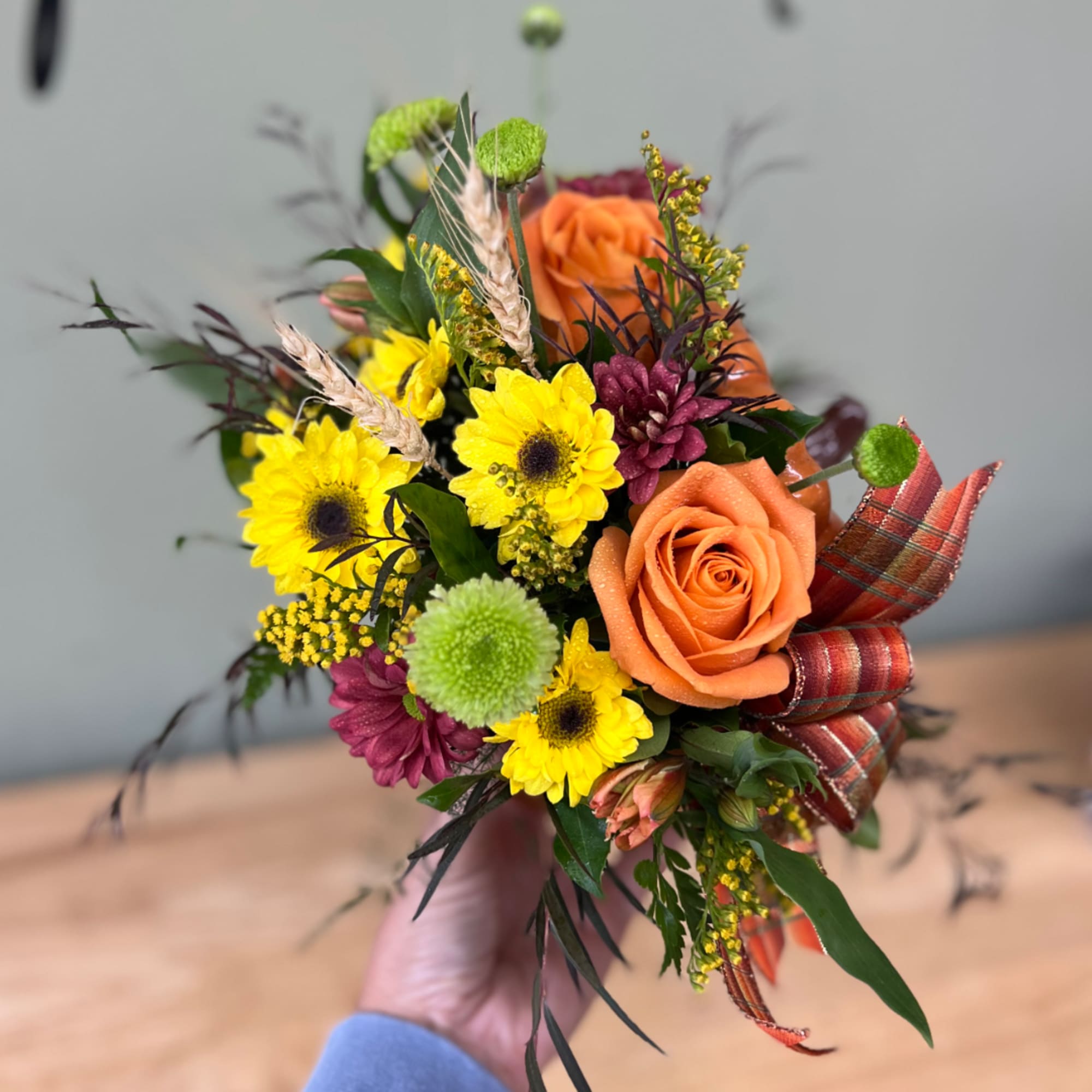 Handheld bouquet with orange roses, yellow daisies, and burgundy blooms
