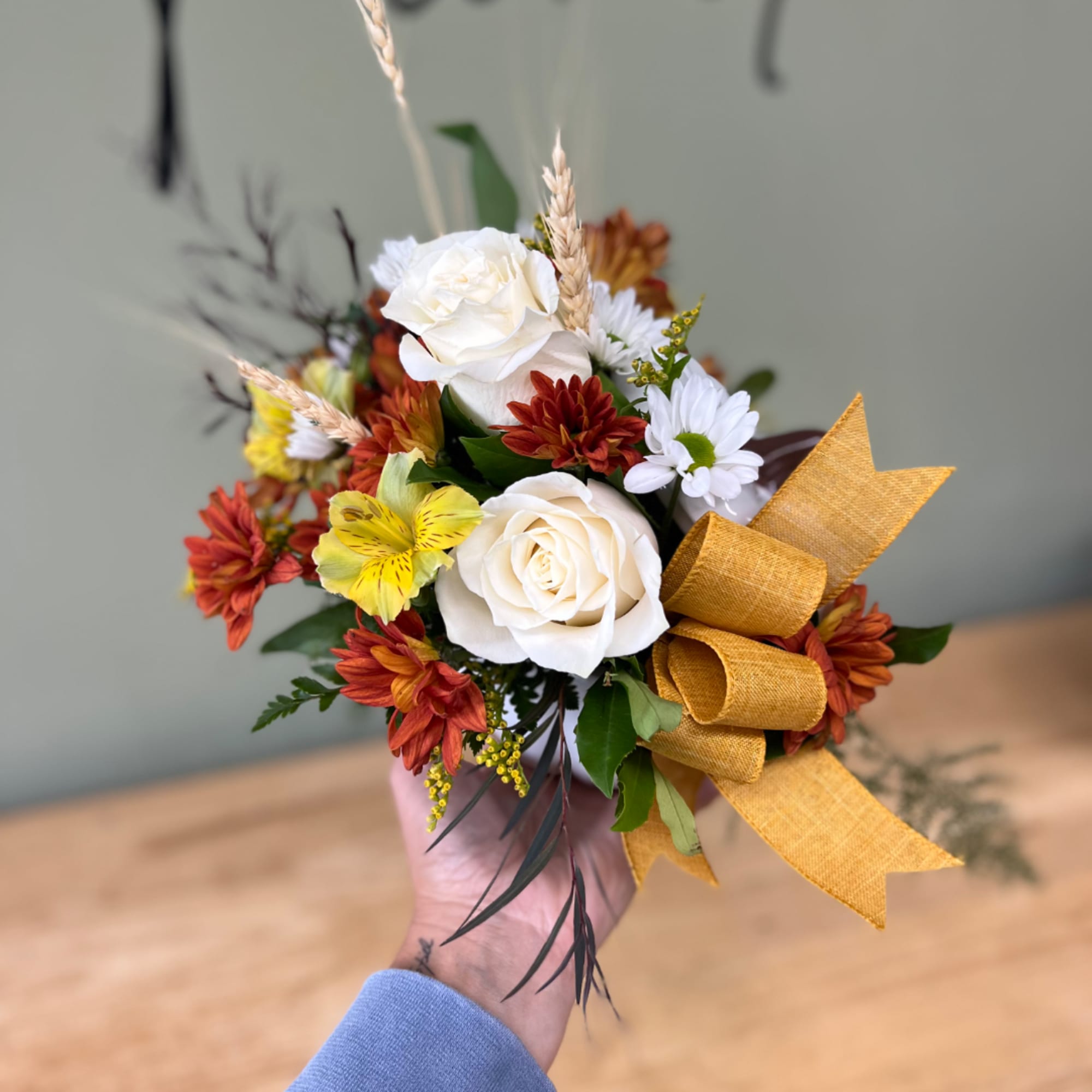 Handheld bouquet of white roses, daisies, and autumn-colored flowers with a gold ribbon