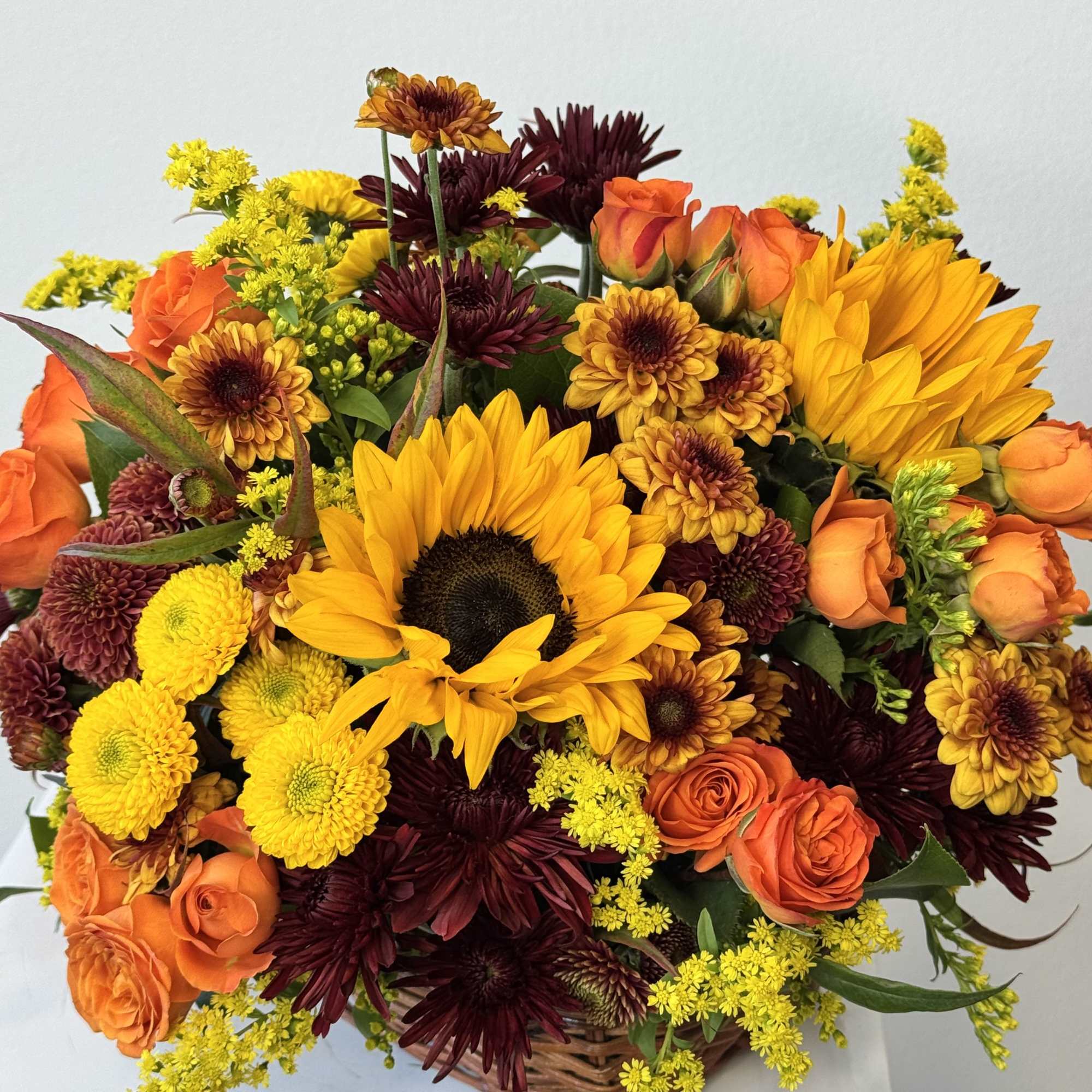 Basket arrangement with sunflowers, orange roses, and burgundy chrysanthemums