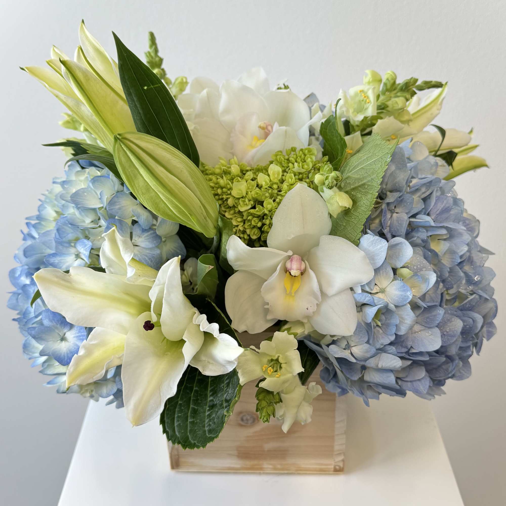 Blue hydrangeas and white orchids arranged in a wooden box