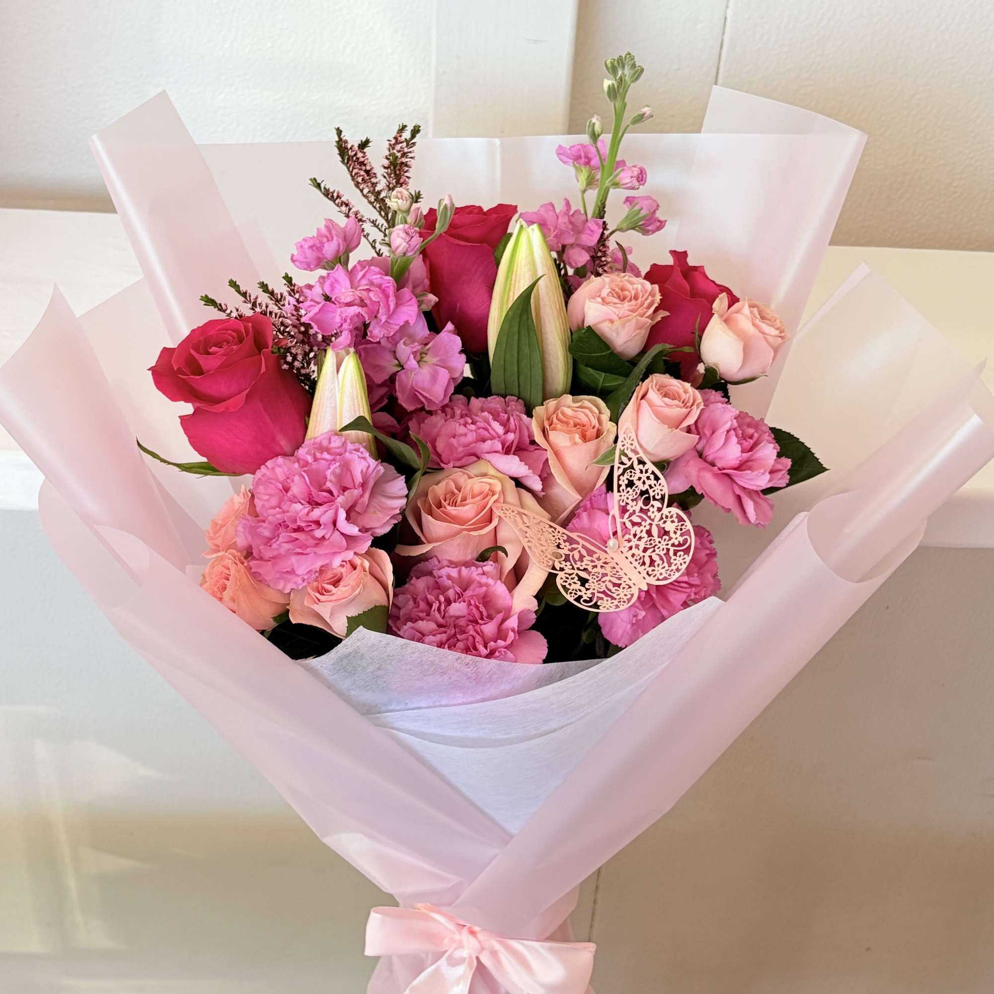 Pink and peach rose bouquet with carnations and lilies in pale pink wrap