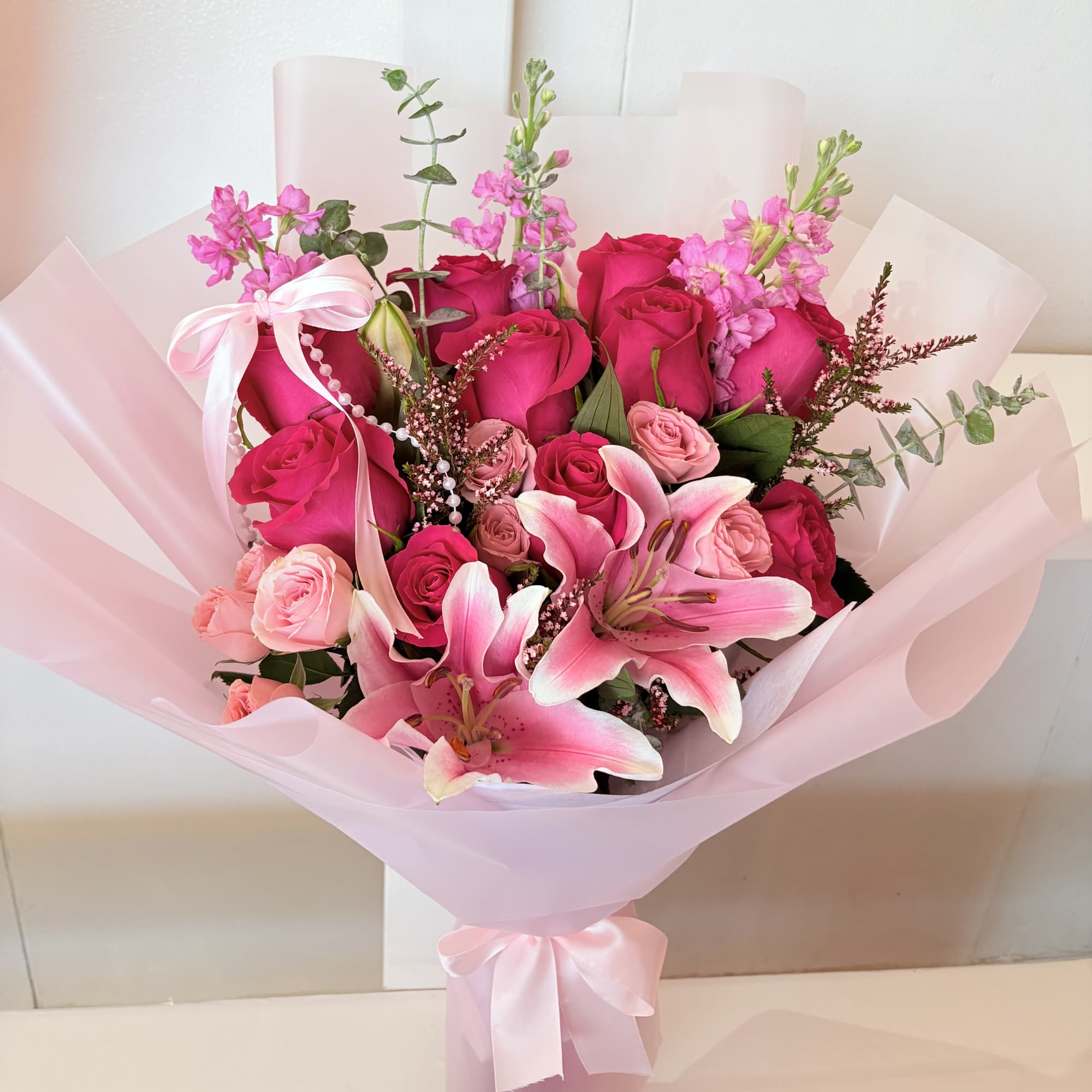 Pink rose and lily bouquet wrapped in pale pink paper with a ribbon