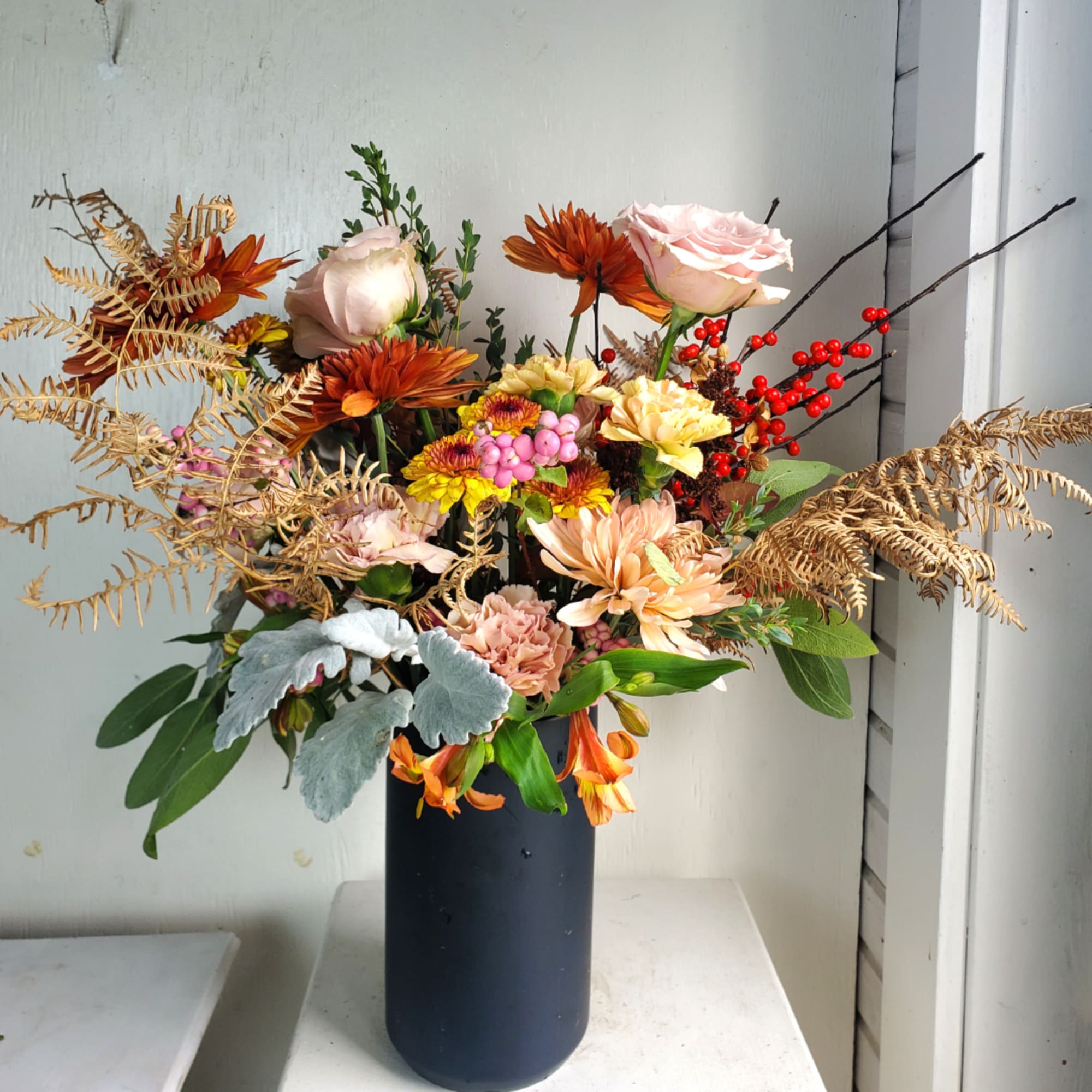 Mixed autumn bouquet in a tall black vase with roses and chrysanthemums