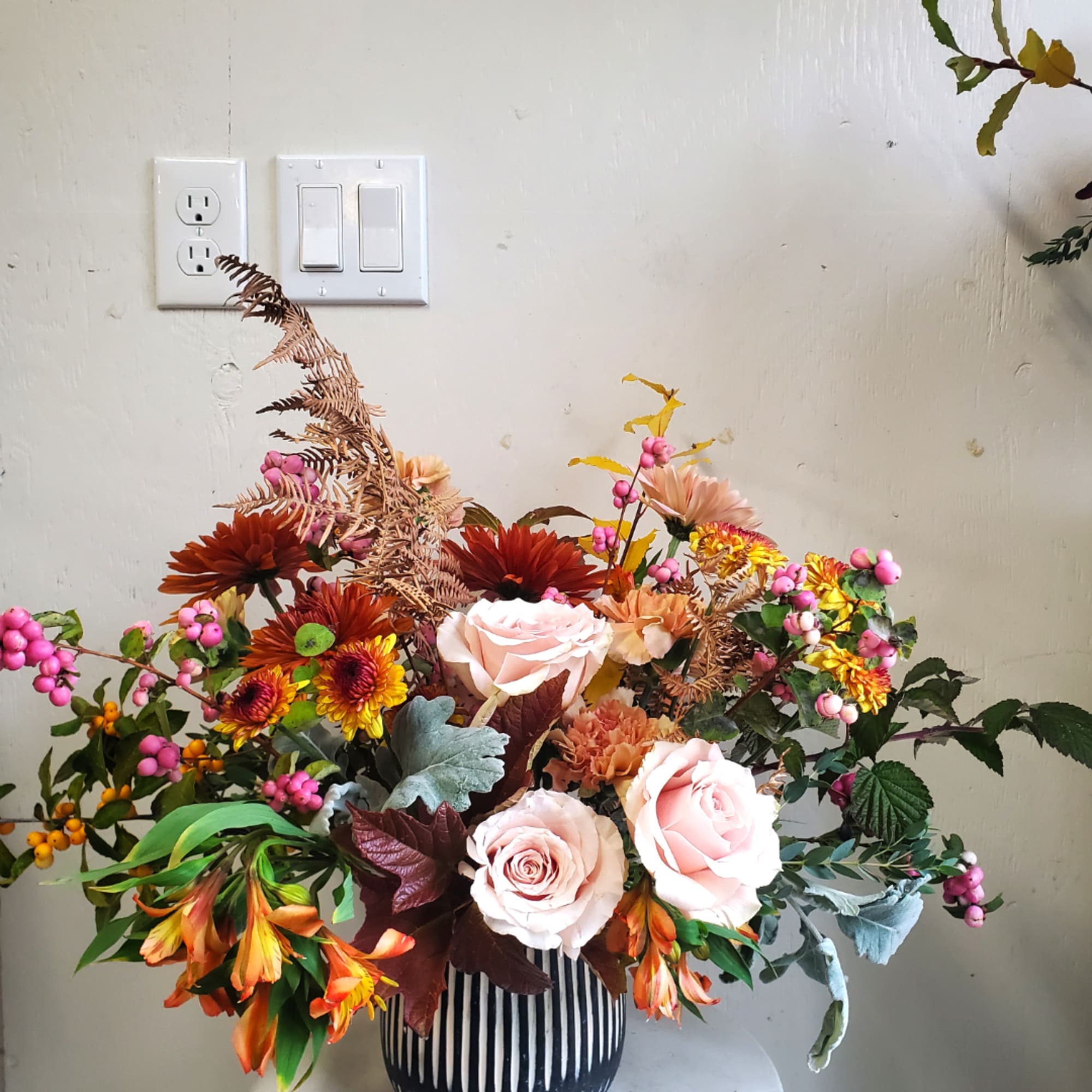 Mixed bouquet with pale pink roses and autumn-colored flowers in a striped vase