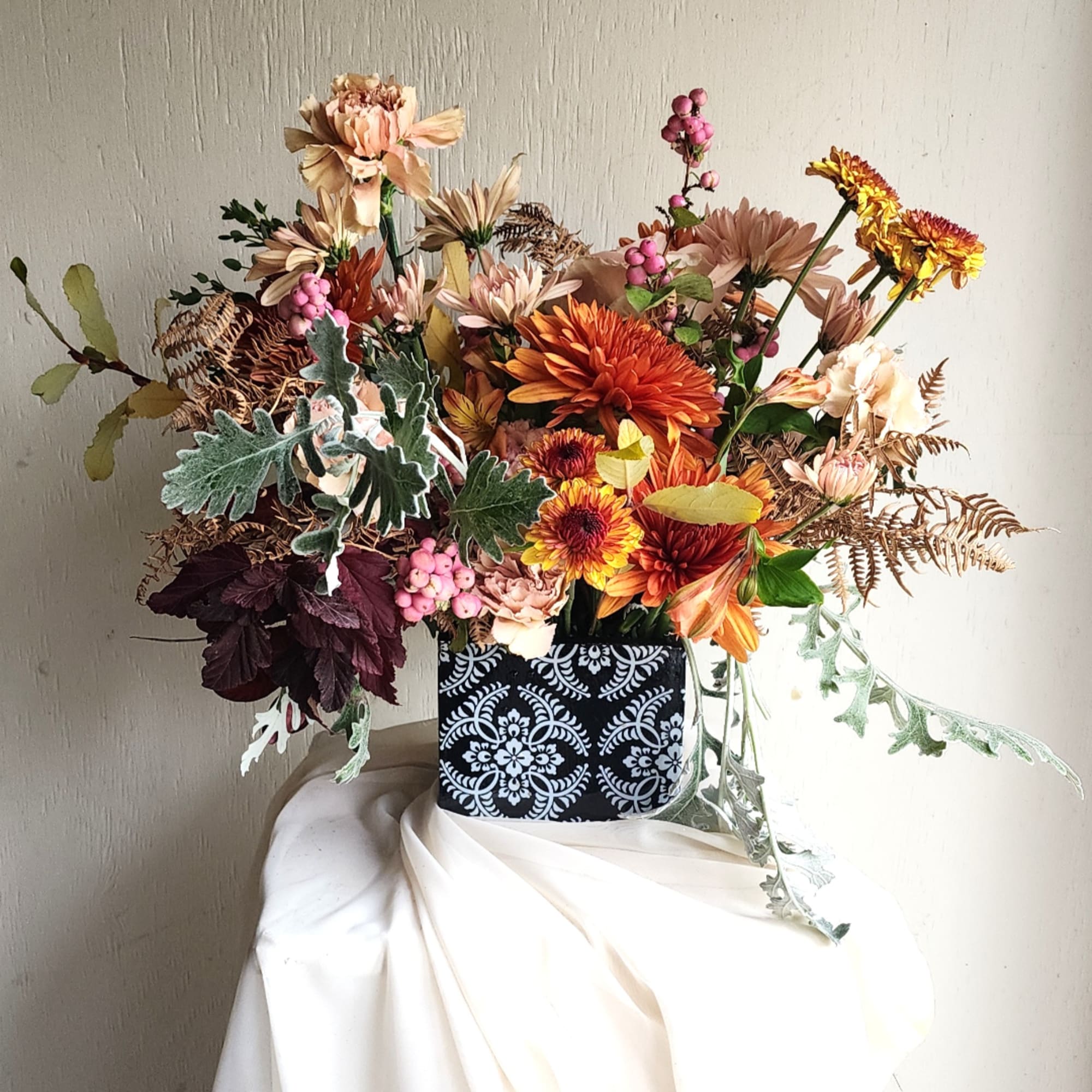 Mixed bouquet of orange and peach flowers in a patterned black container