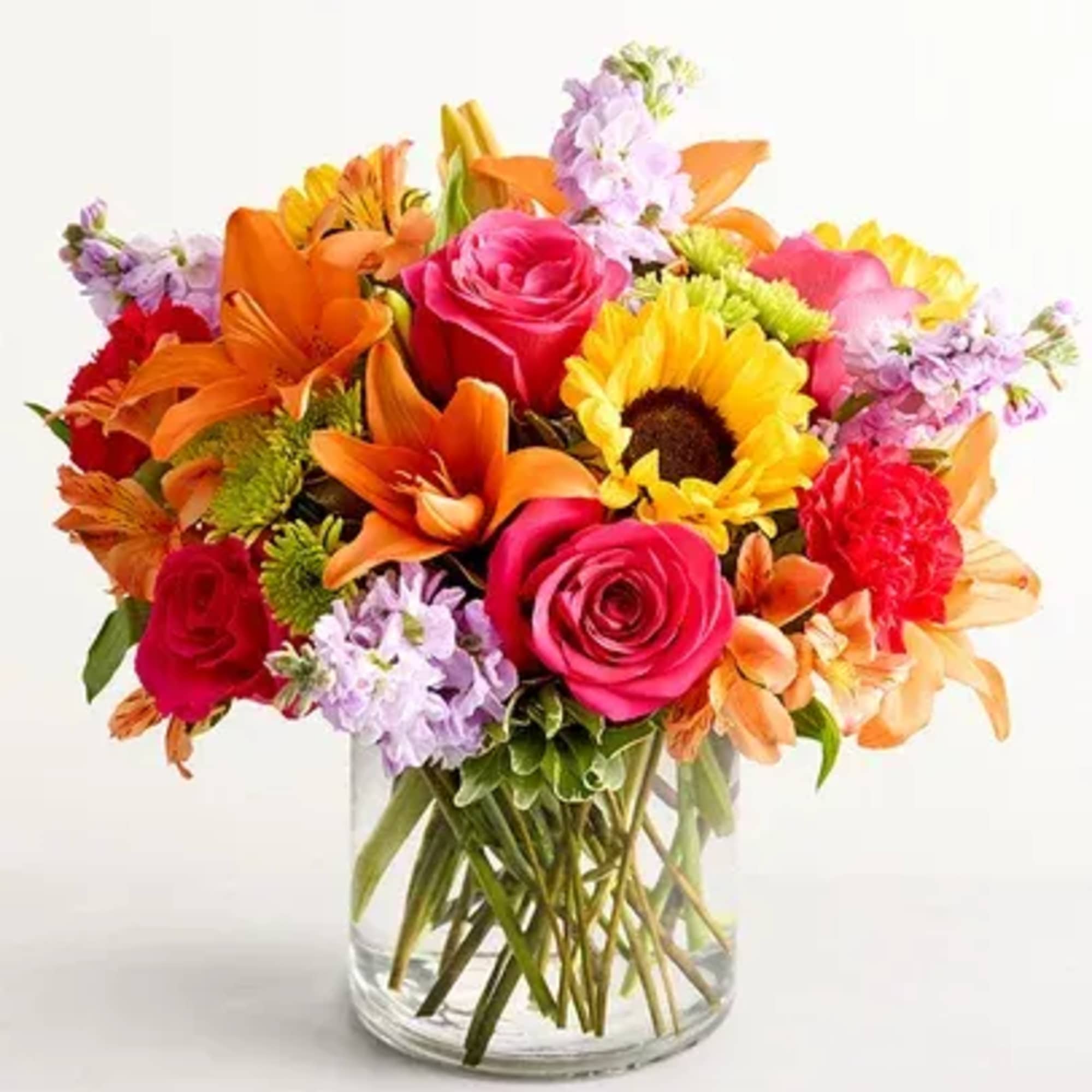 Bright mixed bouquet in a clear glass vase with roses, lilies, and a sunflower