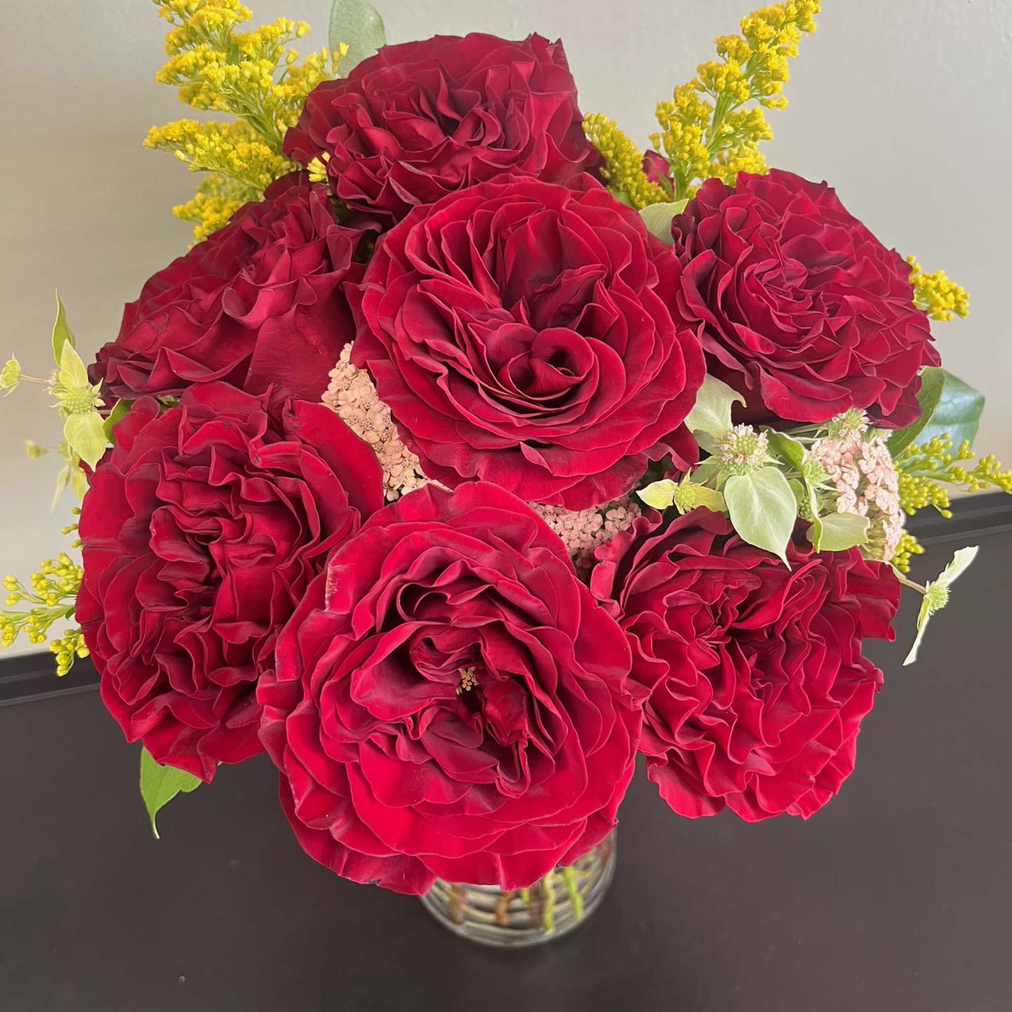 Red rose bouquet in a clear glass vase with yellow filler flowers