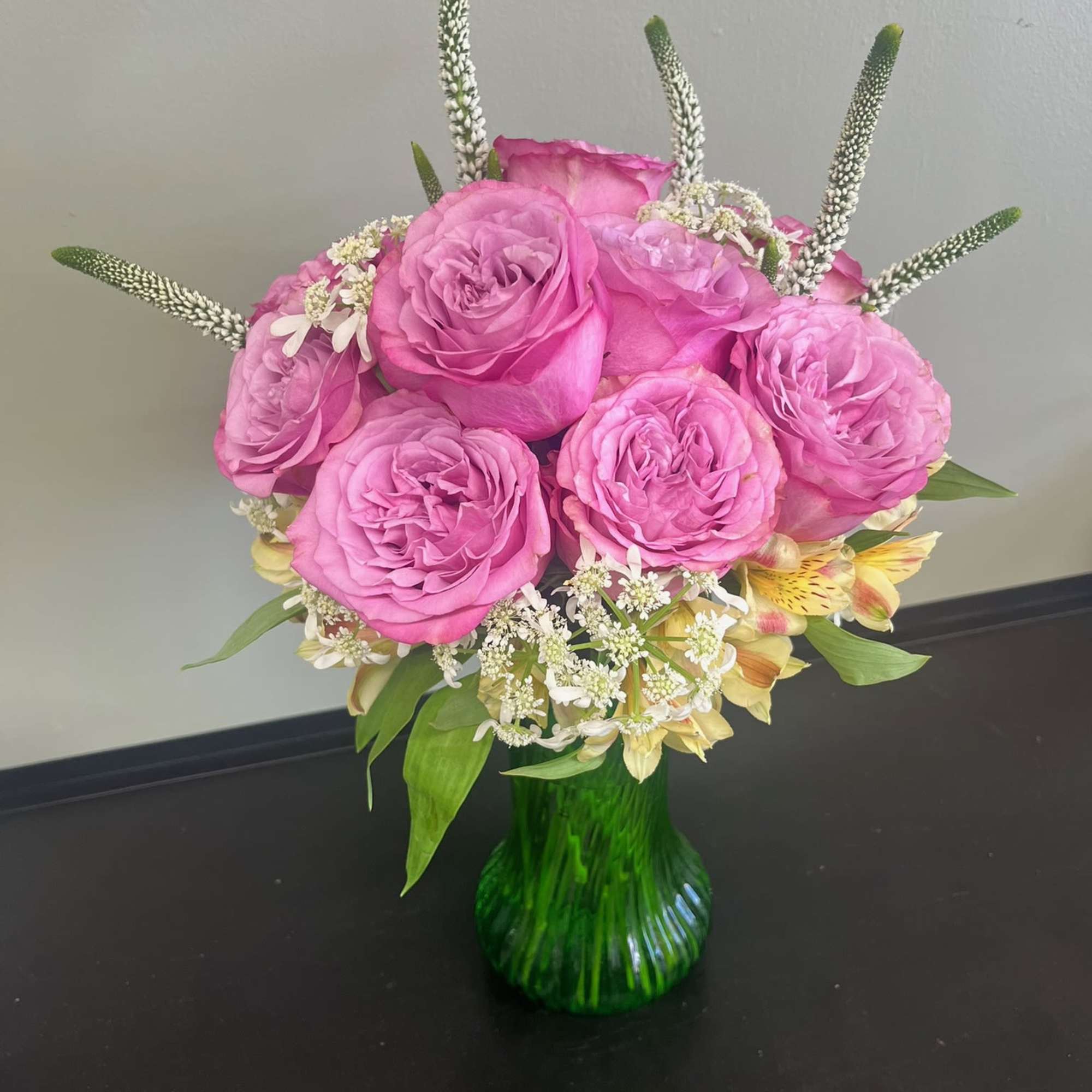 Pink roses arranged in a green glass vase with small white flowers