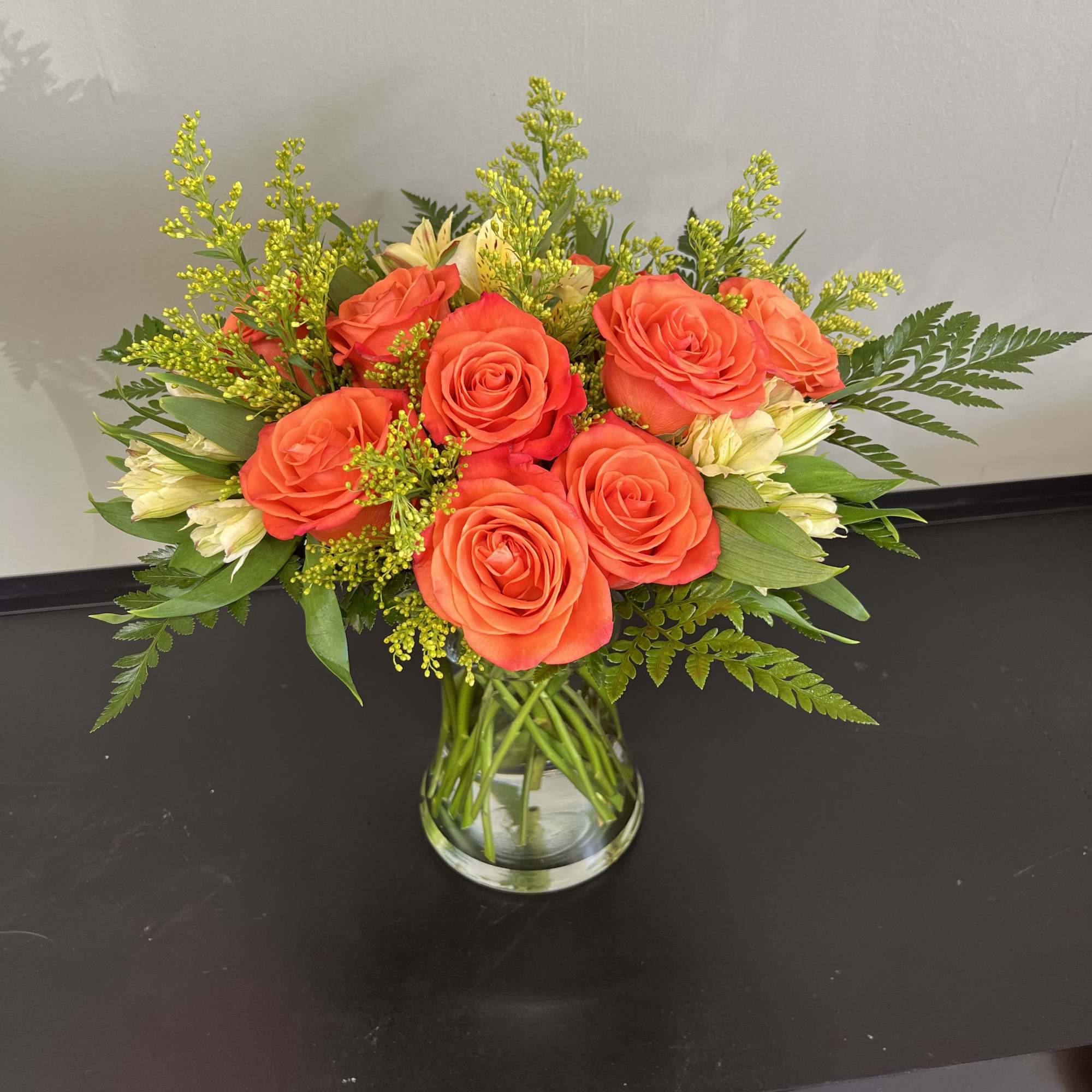 Orange roses arranged in a clear glass vase with yellow filler flowers