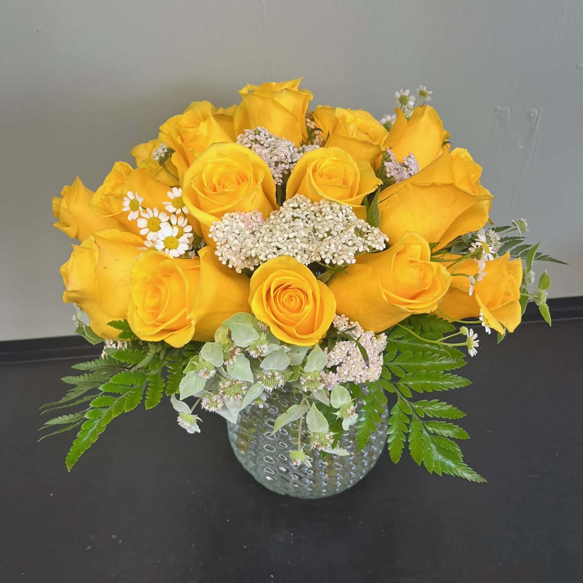 Yellow roses arranged in a glass vase with small white filler flowers