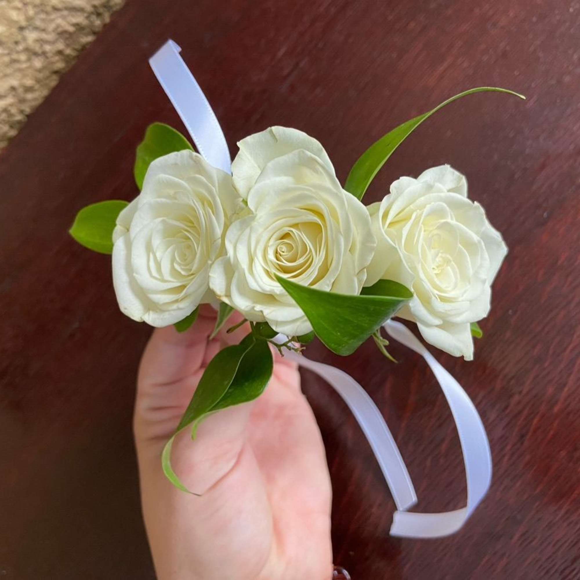 White rose wrist corsage with green leaves and white ribbon