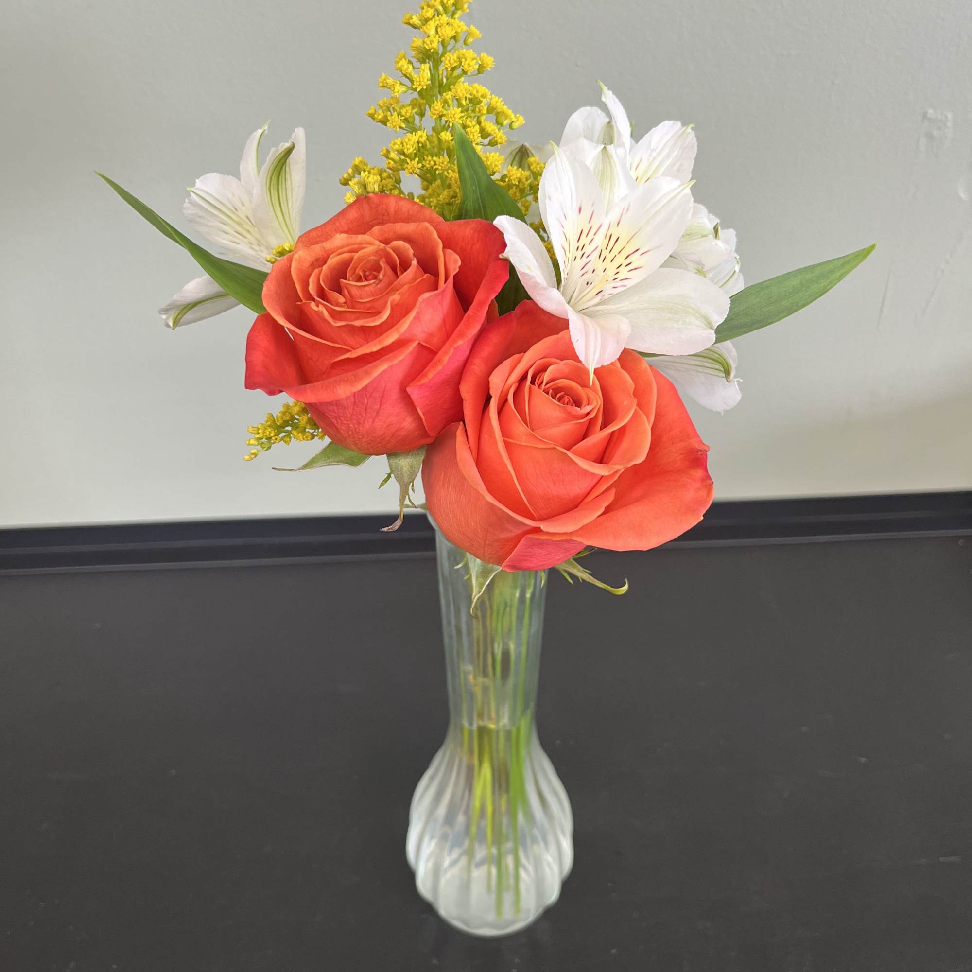 Two coral roses in a clear vase with white alstroemeria and yellow filler flowers