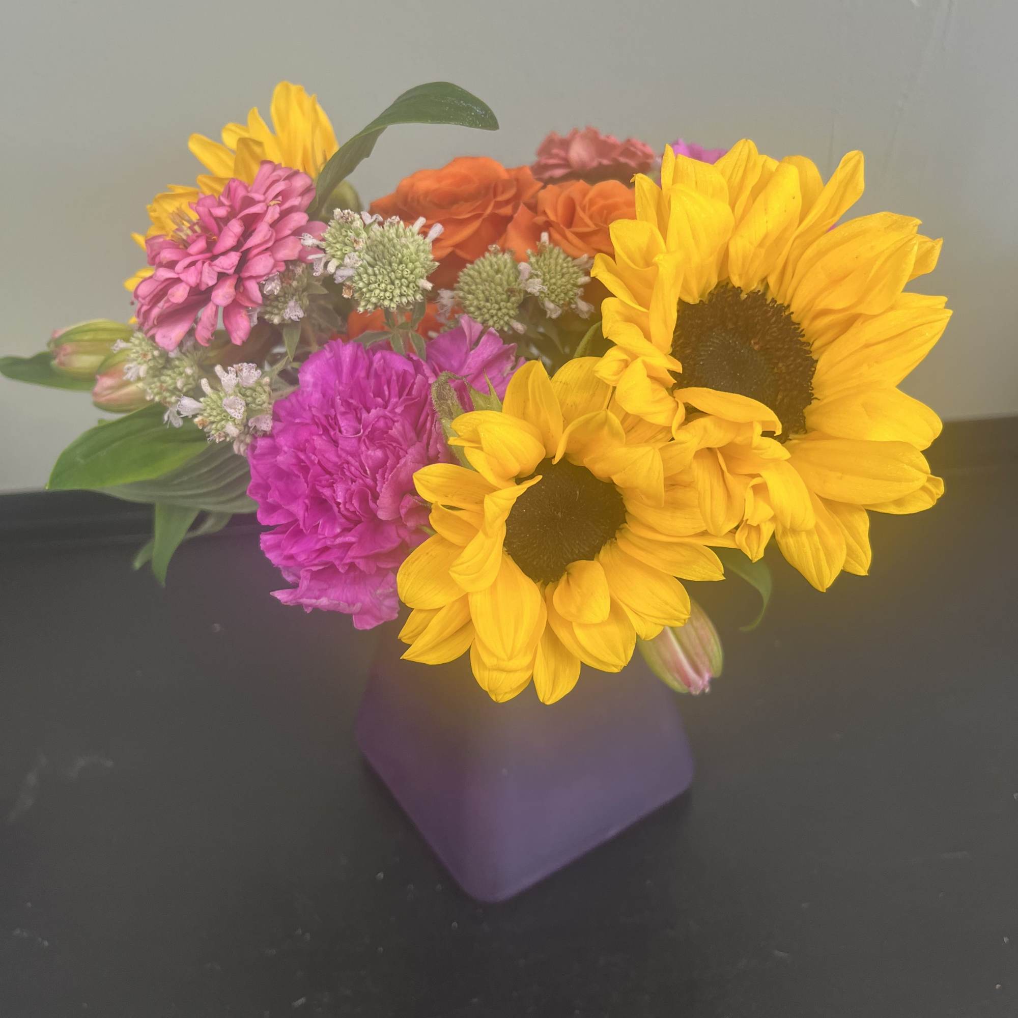 Bright mixed bouquet with sunflowers, pink blooms, and orange roses in a purple vase