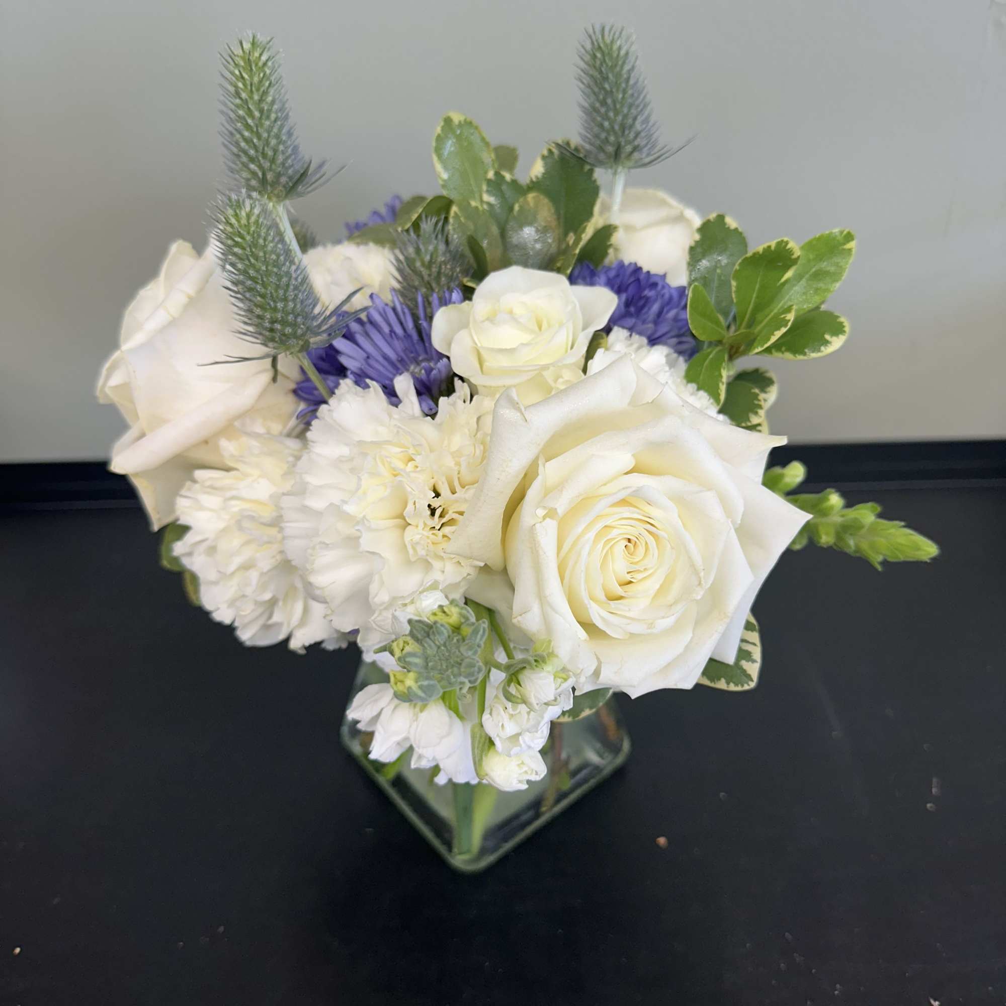 White roses and purple flowers arranged in a square glass vase