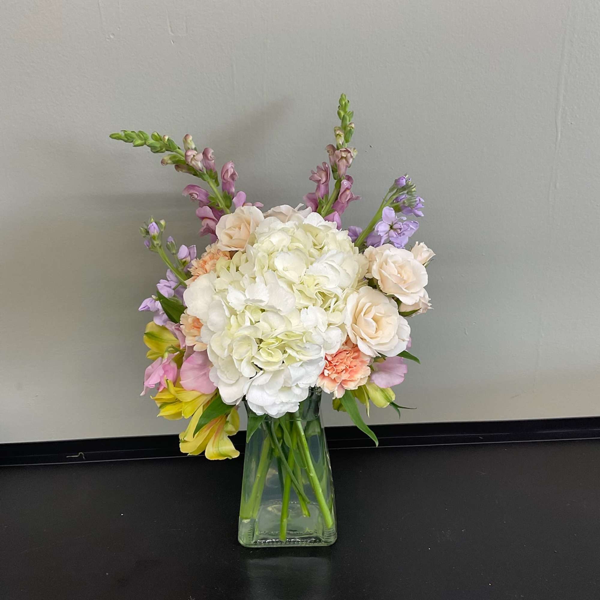 Pastel bouquet of hydrangeas, roses, and snapdragons in a glass vase