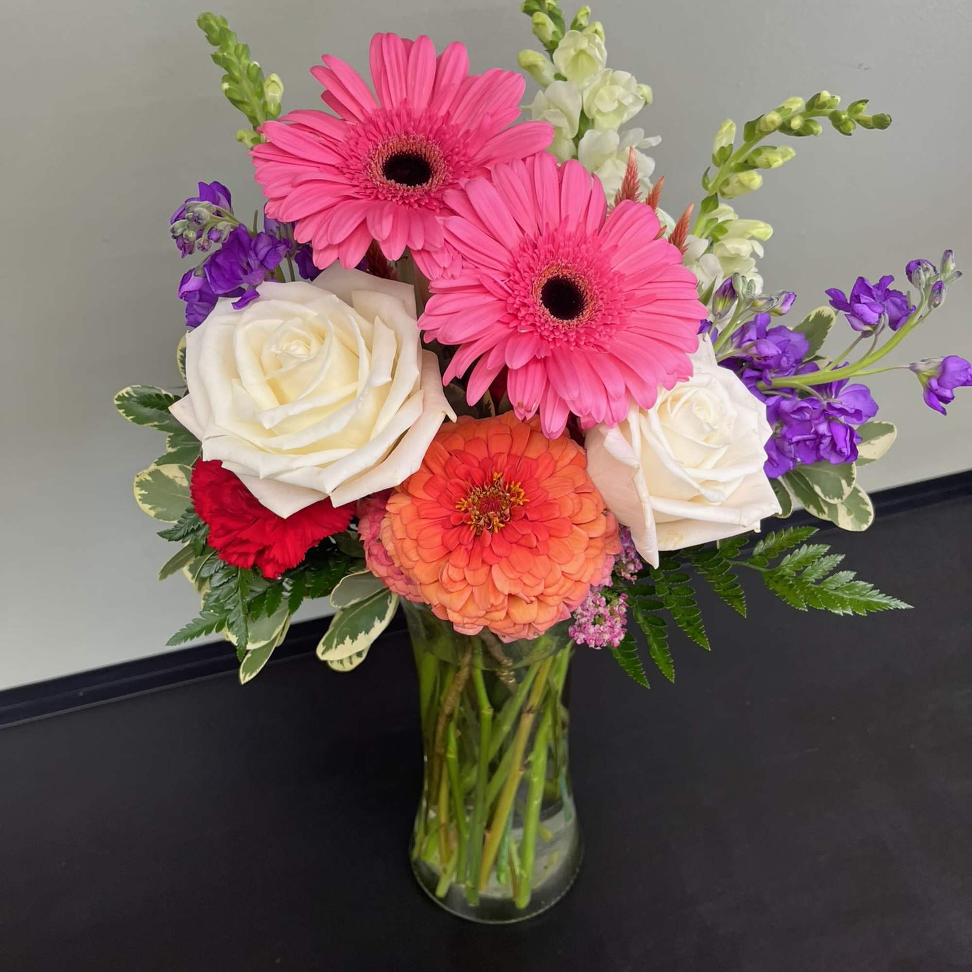 Mixed bouquet with pink gerbera daisies, white roses, and purple blooms in a glass vase
