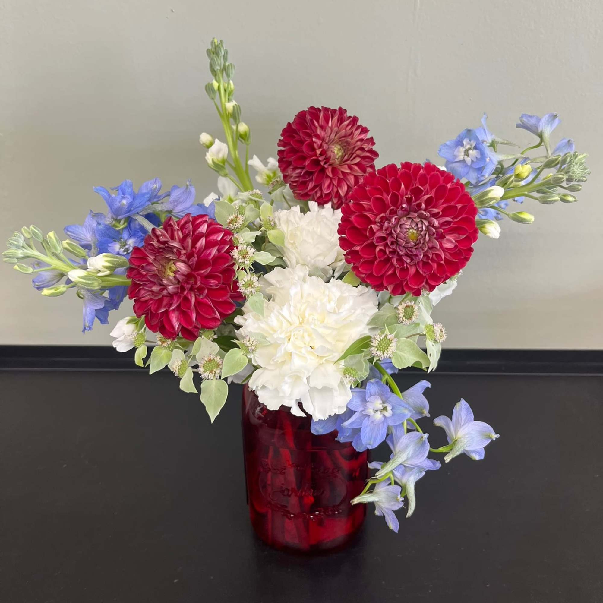 Red and white flowers in a red glass vase with blue accents