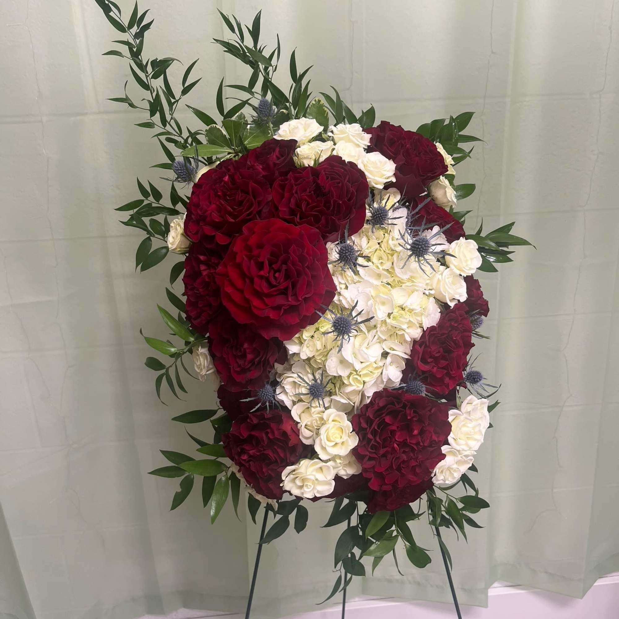 Standing floral spray with deep red and white roses on a metal easel