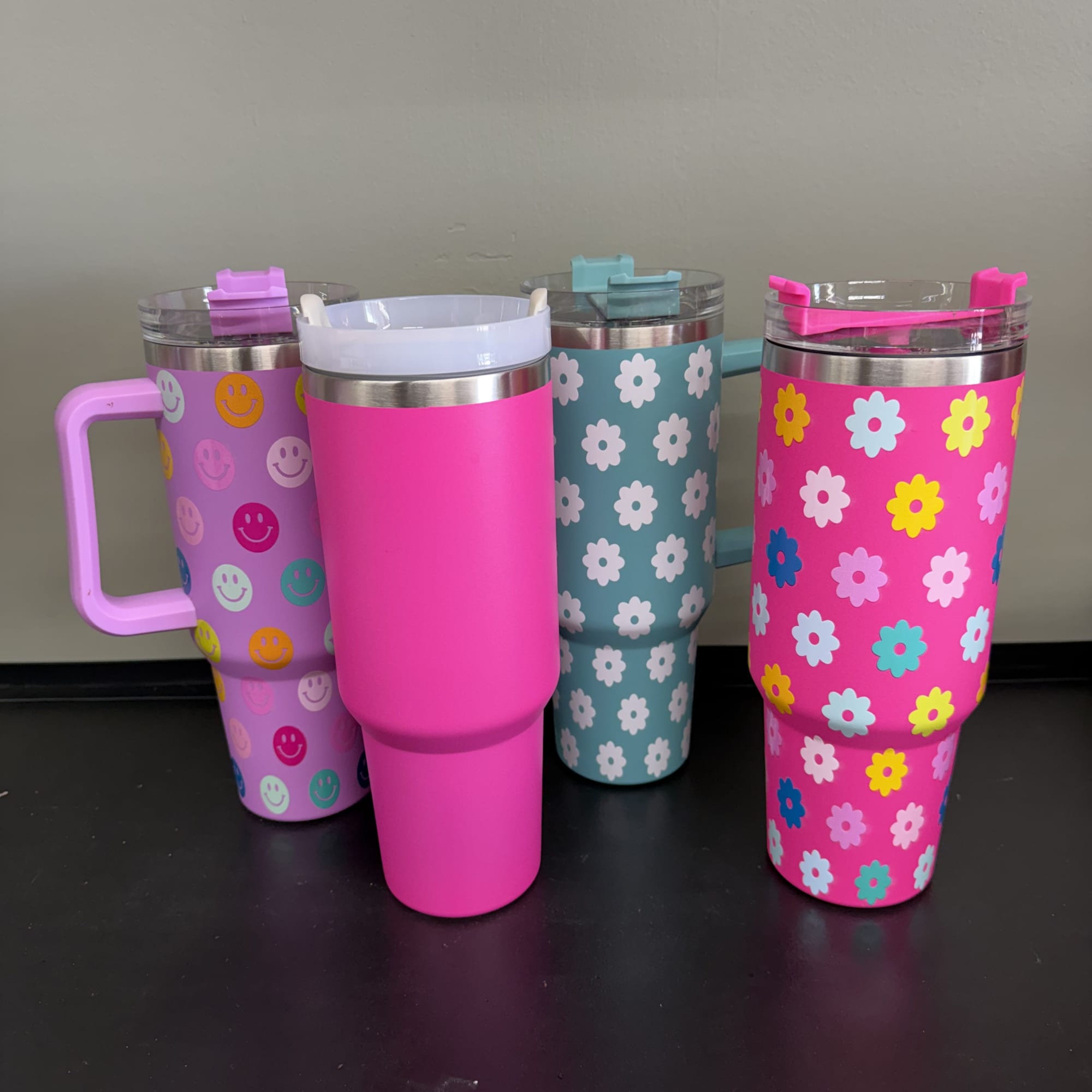 Four colorful insulated tumblers with floral and smiley-face patterns