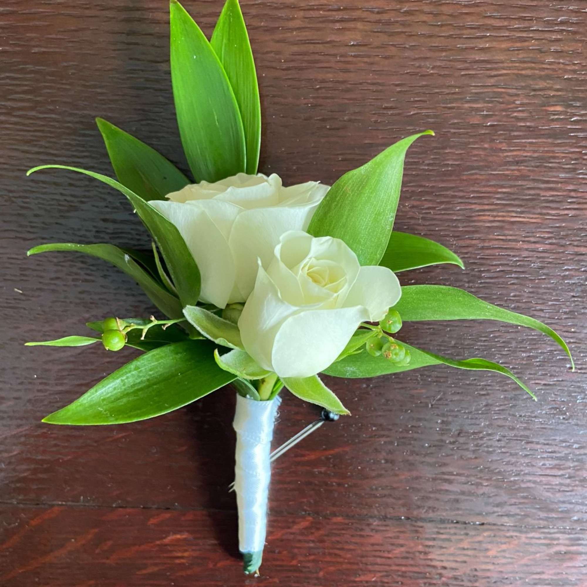 White rose boutonniere with green leaves on a wrapped stem