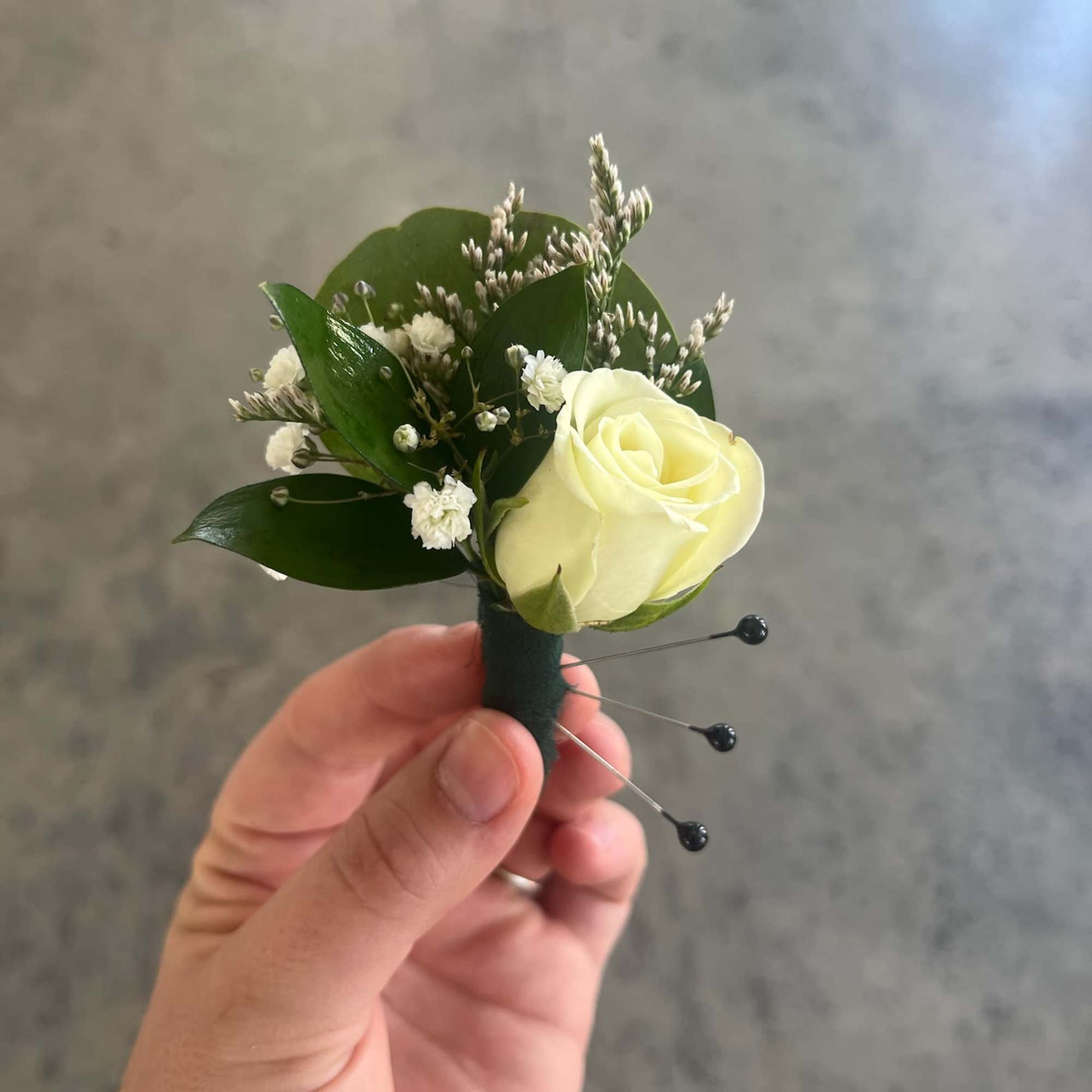 White rose boutonniere with small white filler flowers and dark green leaves