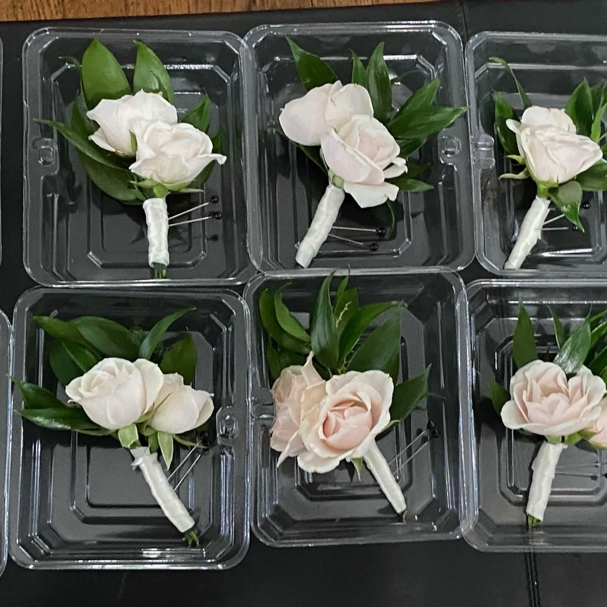 Small pale rose boutonnieres in clear plastic trays