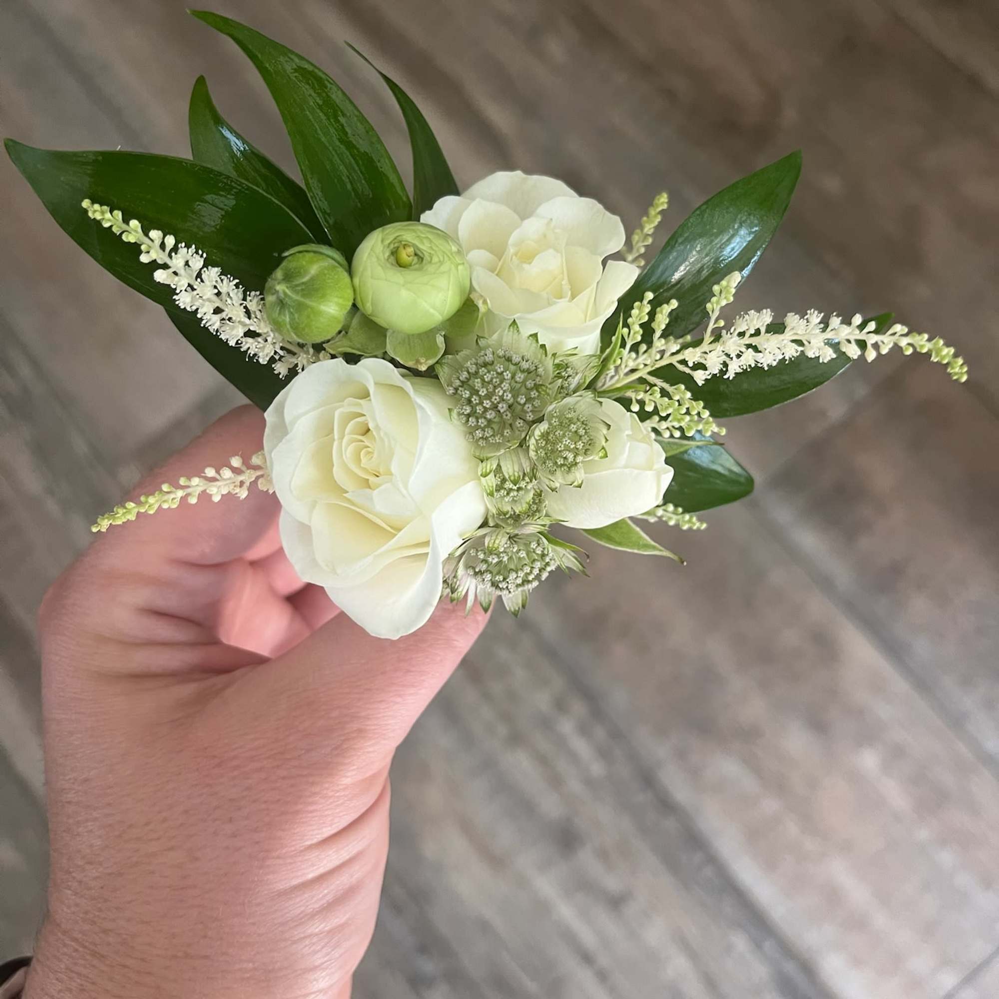 Small white floral corsage with green accents held in hand