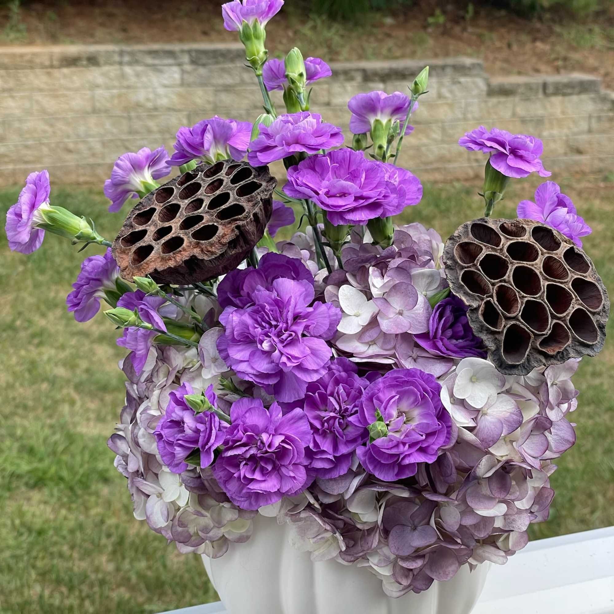 Purple flowers arranged in a white vase with dried seed pods