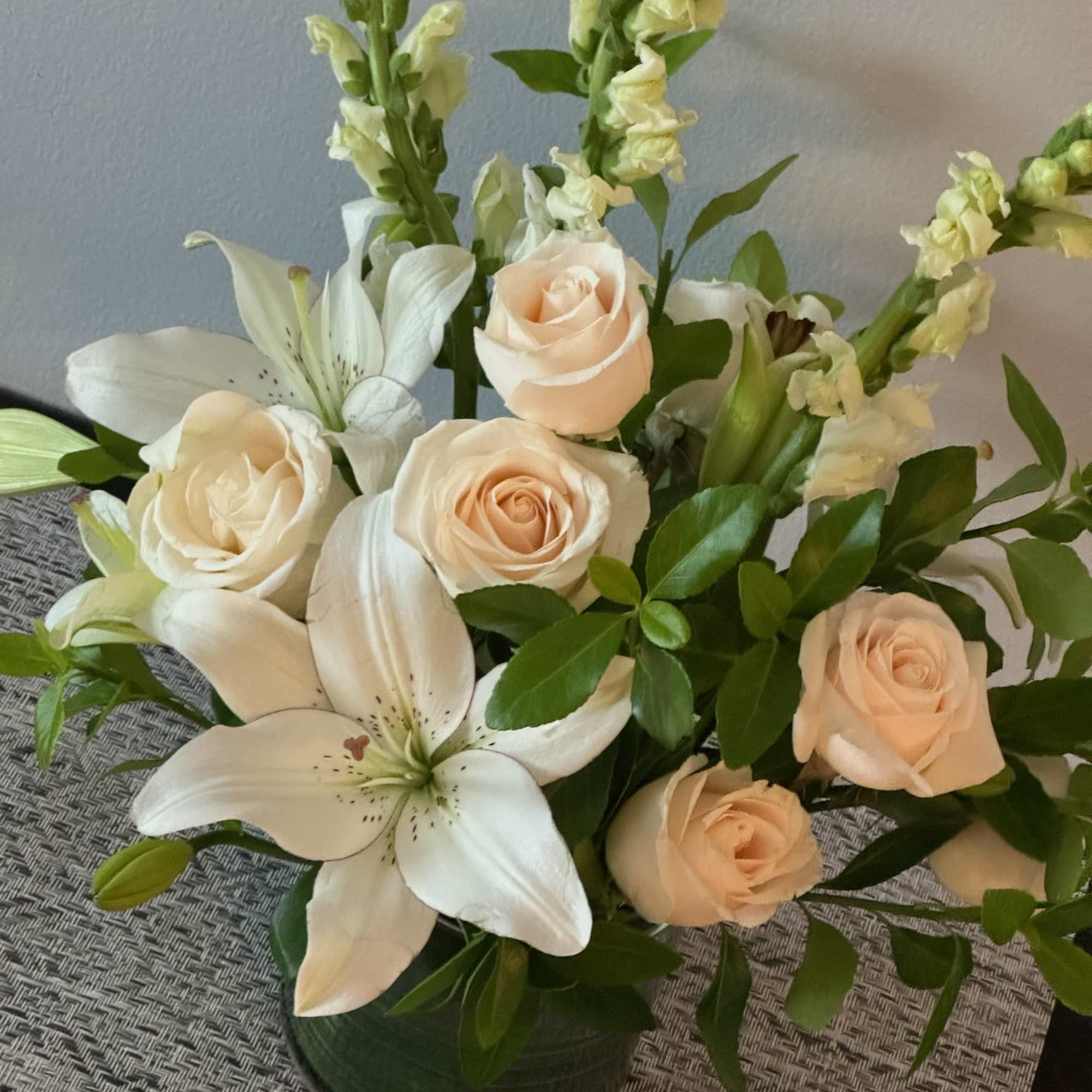 Cream roses and white lilies arranged in a dark vase